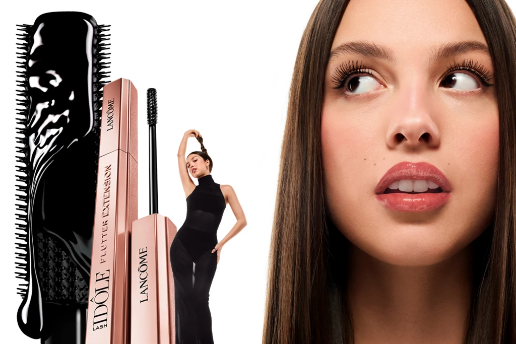 Lancômen Lash Idôle -ripsiväri ja sen harja sekä poseeraava mustapukuinen nainen. Taustalla on lähikuva pitkistä, suorista hiuksista.