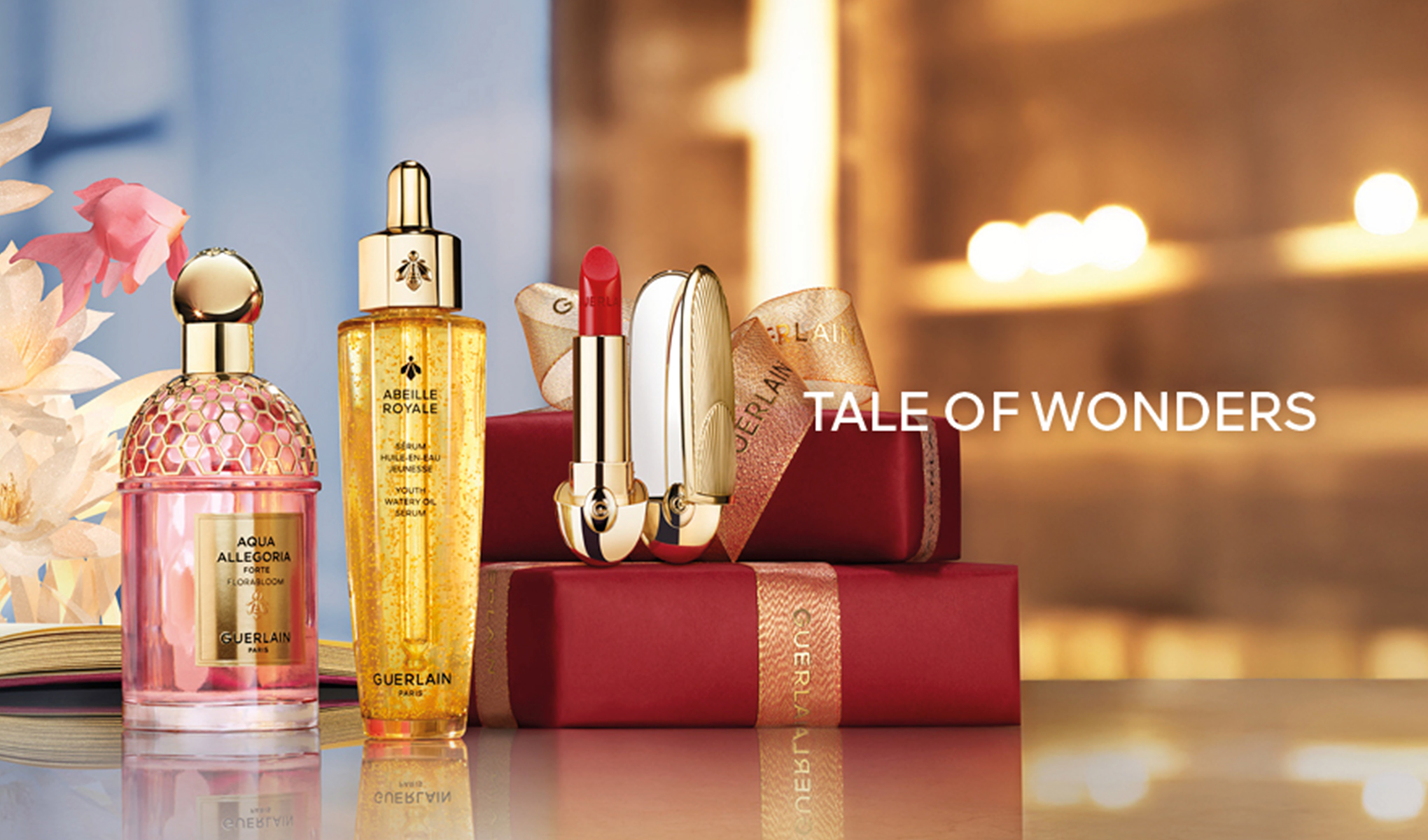 Guerlain-reklame med Aqua Allegoria-parfyme, Abeille Royale-serum og en rød leppestift. I bakgrunnen er det gaveesker og teksten "Tale of Wonders".