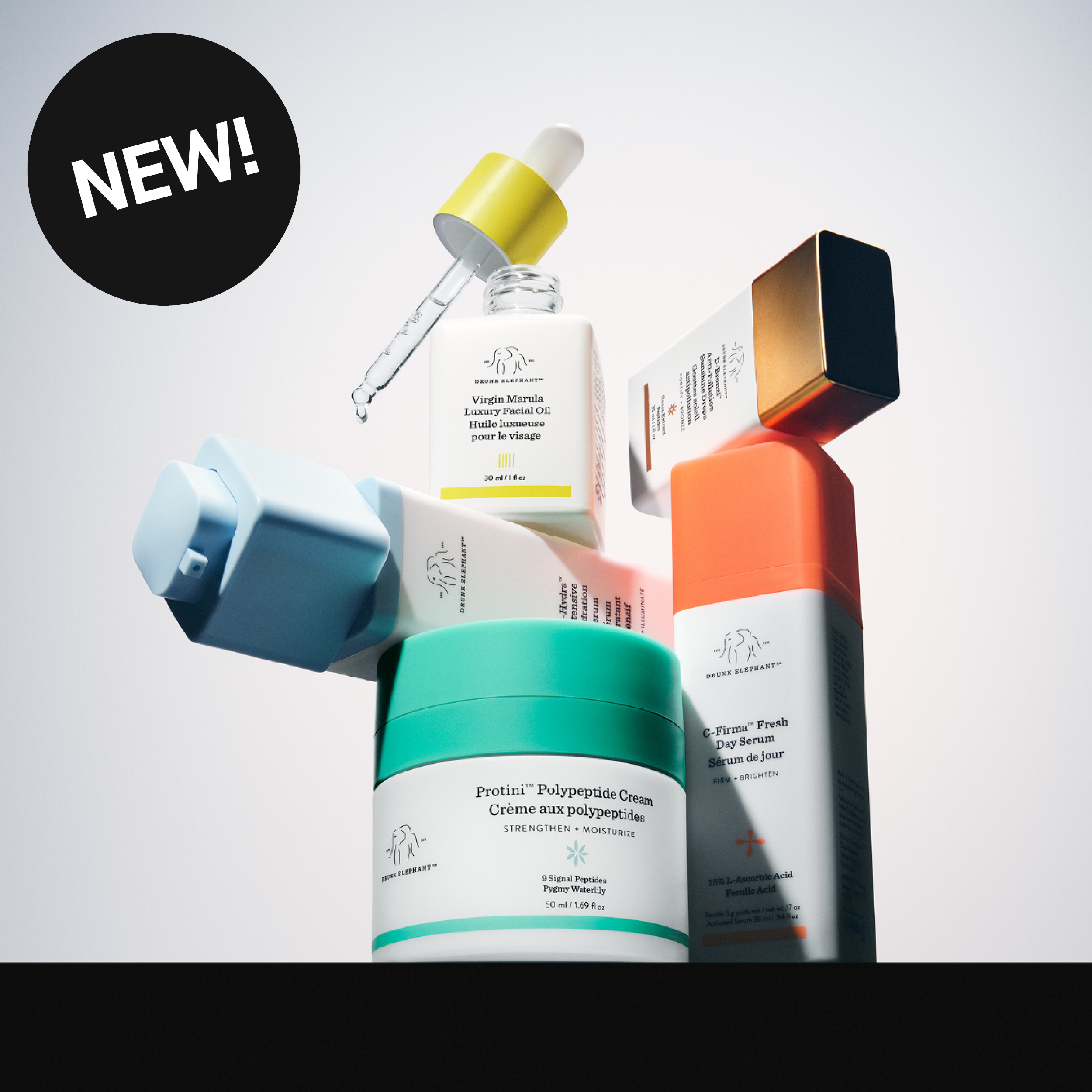 Drunk Elephant -ihonhoitotuotteita kuten “Virgin Marula Luxury Facial Oil”, “Protini Polypeptide Cream” ja “C-Firma Fresh Day Serum”, sekä musta ympyrä tekstillä “NEW!”.