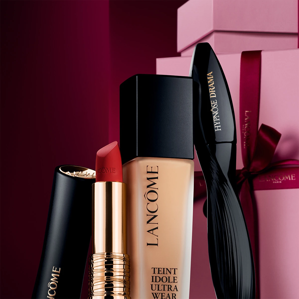 Lancôme skjønnhetsprodukter: rød leppestift, Teint Idole Ultra Wear foundation og Hypnôse Drama mascara, foran rosa gaveesker.