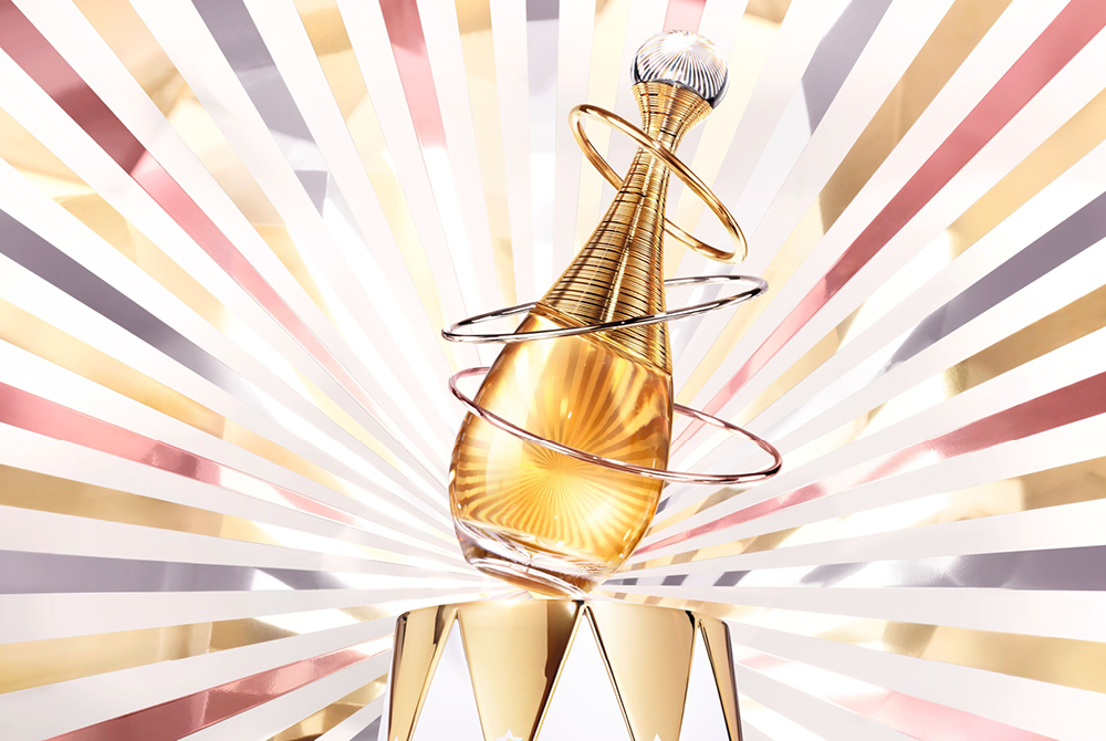 Dior J’adore naisten hajuvesi kultaisessa pullossa, valkoisen ja ruusukullan sävyinen tausta.