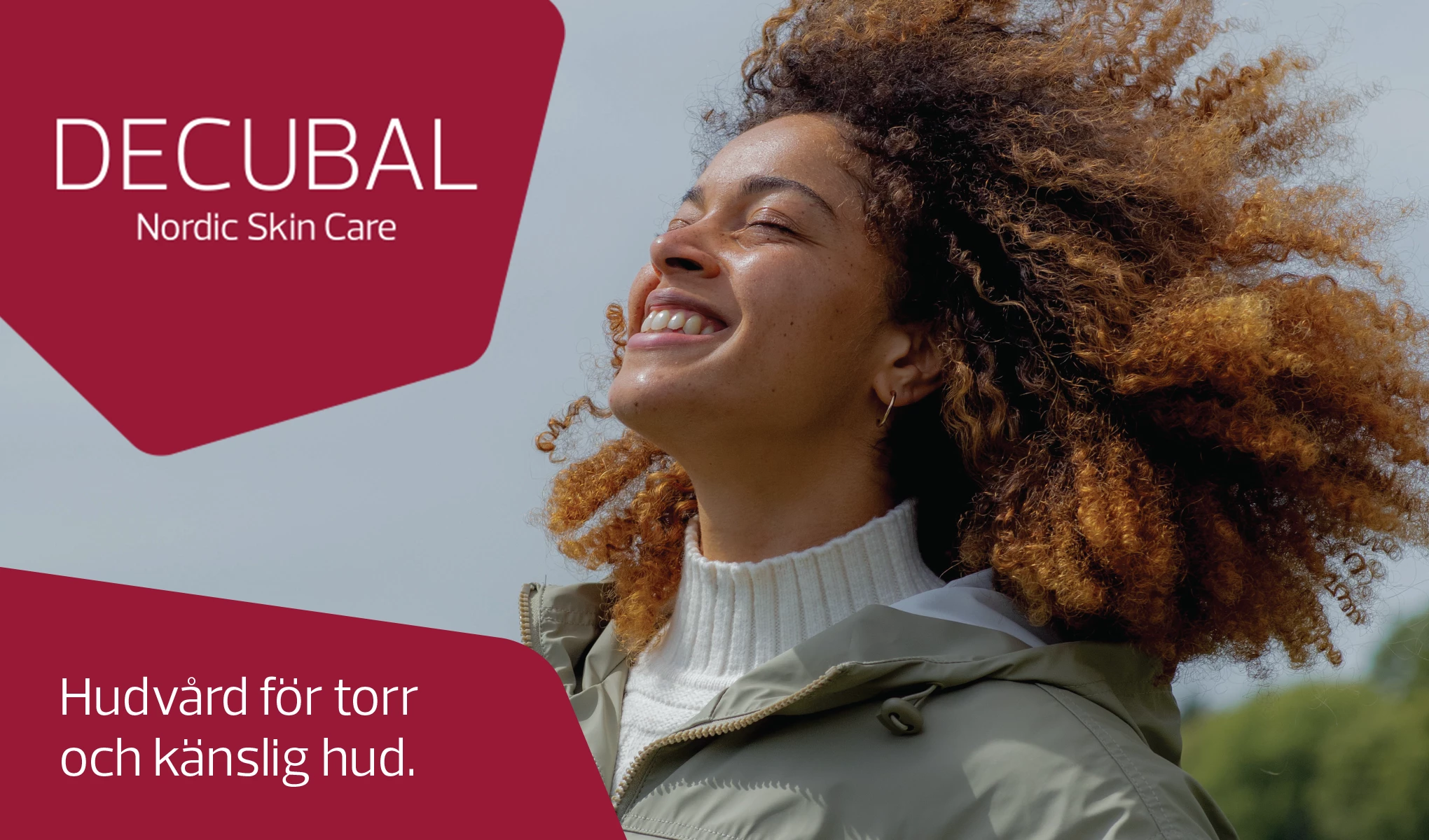 En person med krøllete, brunt hår står ute i naturen, iført en hvit genser og en grønn jakke. Det står "DECUBAL Nordic Skin Care. Hudvård för torr och känslig hud." på bildet.