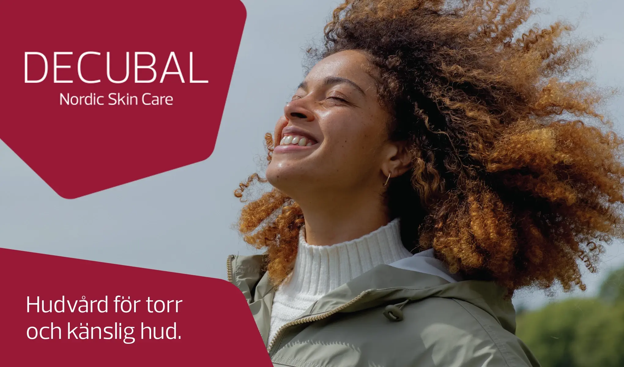 En person med krøllete, brunt hår står ute i naturen, iført en hvit genser og en grønn jakke. Det står "DECUBAL Nordic Skin Care. Hudvård för torr och känslig hud." på bildet.