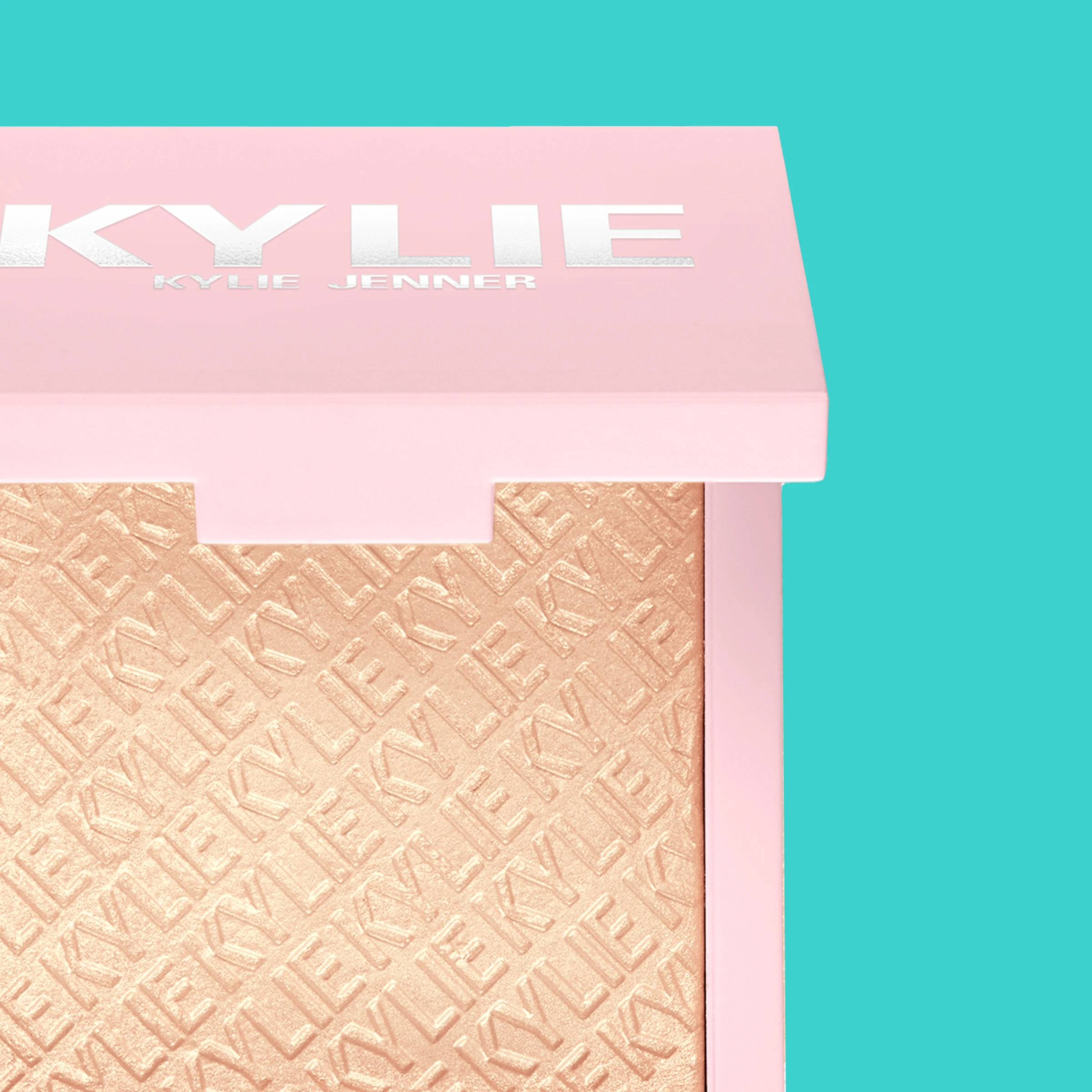 Nærbilde av highlighter i rosa emballasje mot turkis bakgrunn. Preget produktflate. Tekst på lokket: «KYLIE».