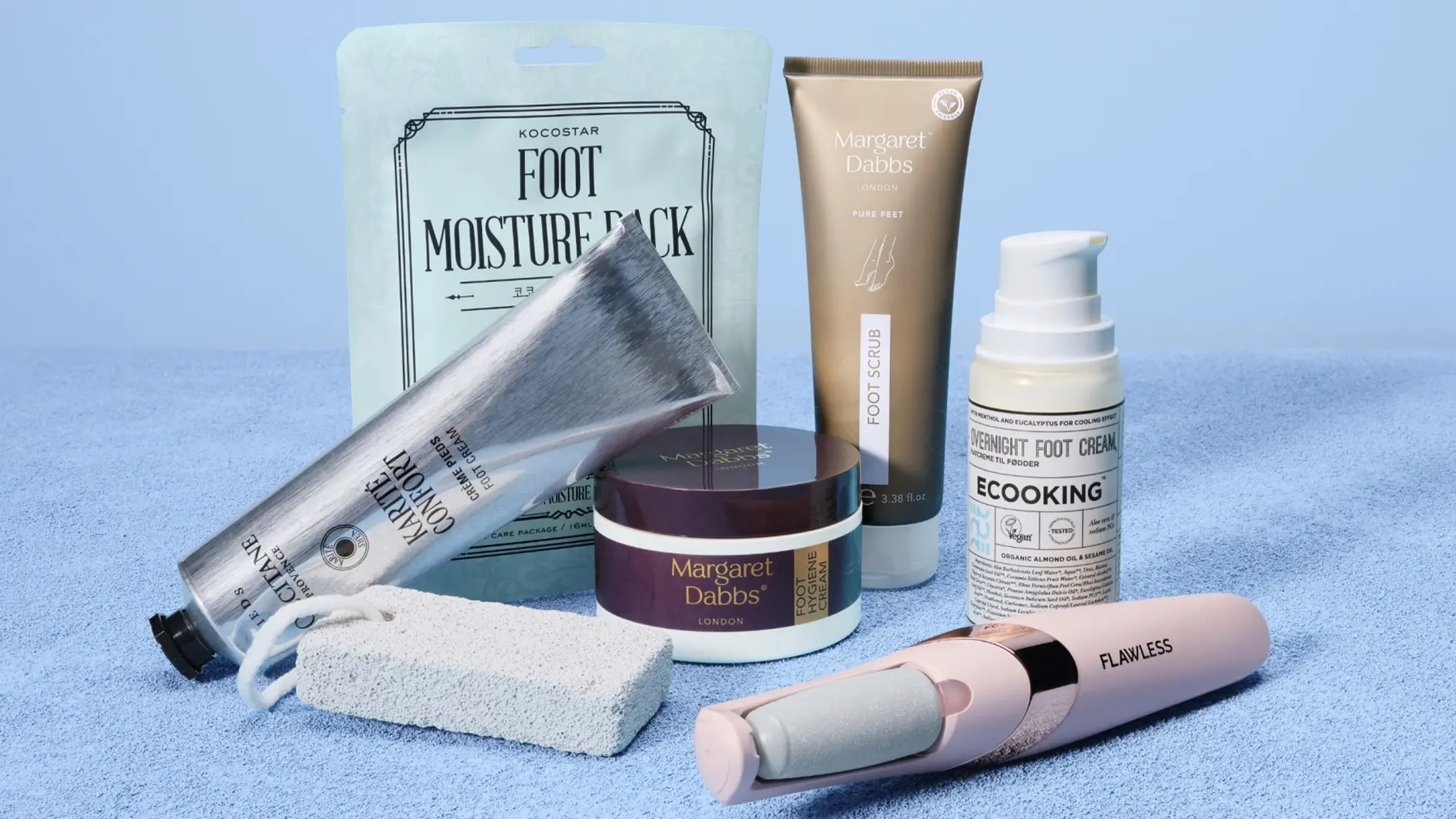 Jalkojenhoitotuotteita vaaleansinistä taustaa vasten, mukana KOCOSTAR Foot Moisture Pack -jalkanaamio, Margaret Dabbs Foot Scrub ja Intensive Hydrating Foot Lotion sekä COOKING Underfoot Foot Cream. Kuvassa näkyy myös Flawless-sähköinen jalkaviila, hopeinen jalkavoidetuubi ja valkoinen hohkakivi kuorivaan ja pehmentävään jalkojenhoitoon kotona.
