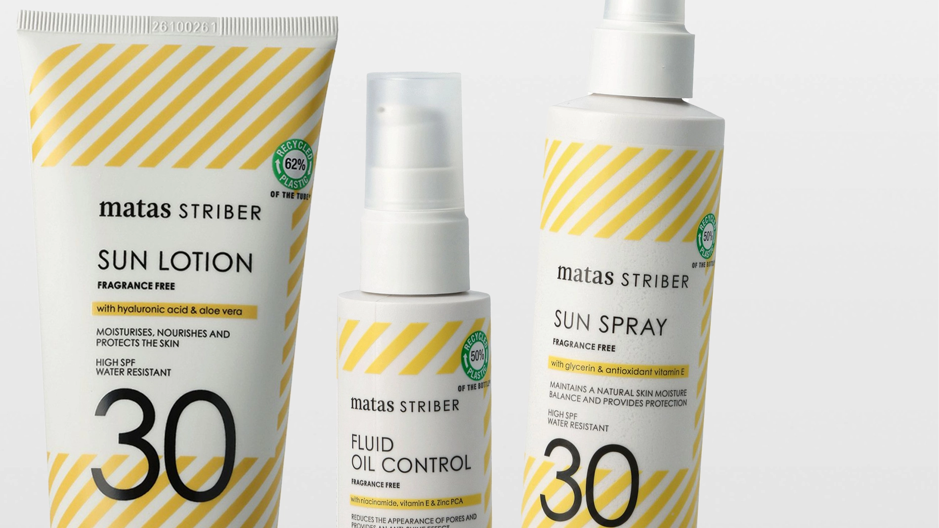 Tre solbeskyttelsesprodukter fra Matas Striber: en tube “SUN LOTION”, en pumpeflaske “FLUID OIL CONTROL” og en sprayflaske “SUN SPRAY”, alle med gule diagonale striper og teksten “FRAGRANCE FREE”. Emballasjen viser “with hyaluronic acid & aloe vera”, “with glycerin and antioxidant vitamin E”, “HIGH SPF 30”, “WATER RESISTANT” samt merkinger som “RECYCLED 62% PLASTIC” og “RECYCLED 50% PLASTIC”.