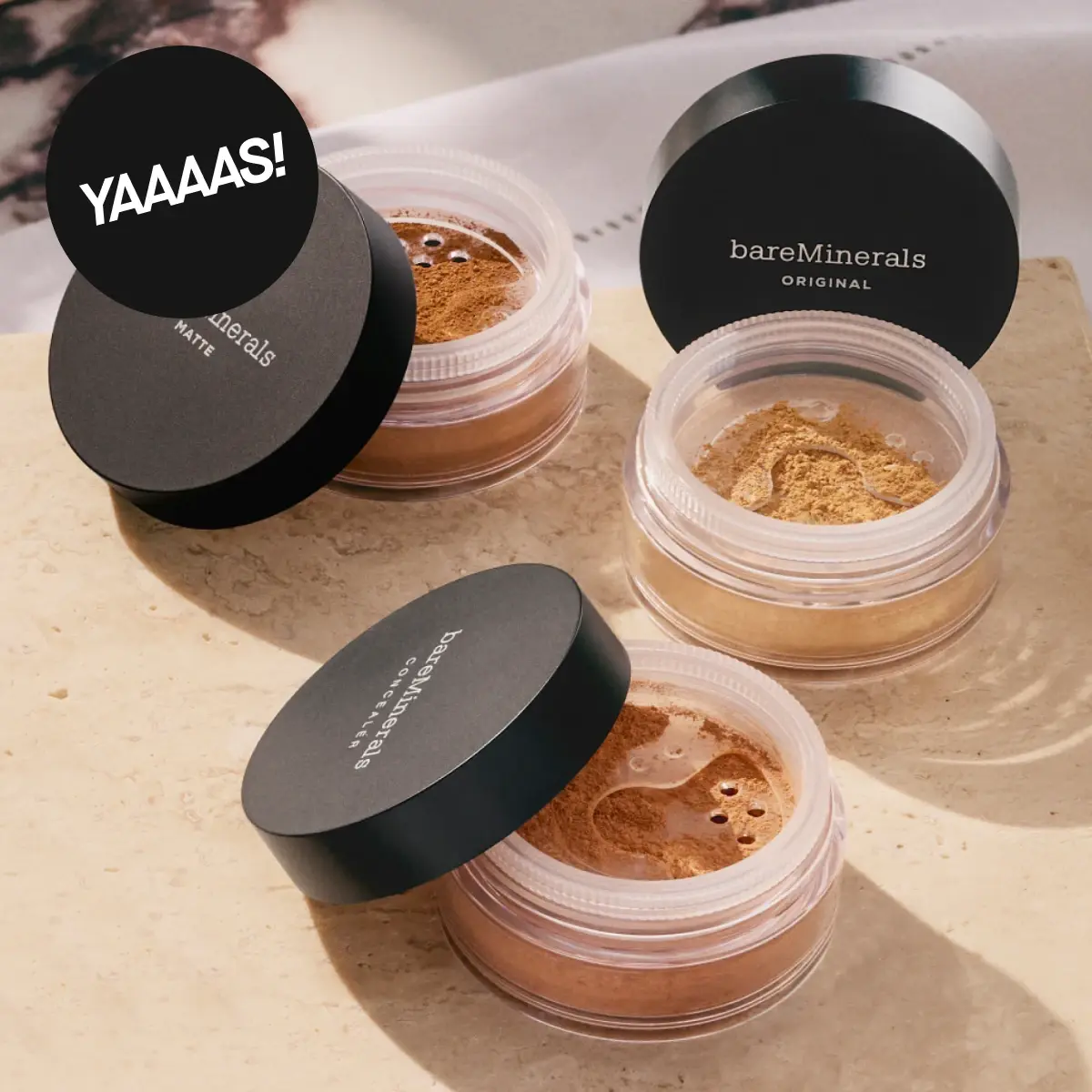 YAAAAS! bareMinerals Original- ja bareMinerals Original Matte -irtomineraalipuuterit useissa sävyissä avoimissa purkeissa, joissa on mustat kannet, beigellä kivipinnalla.
