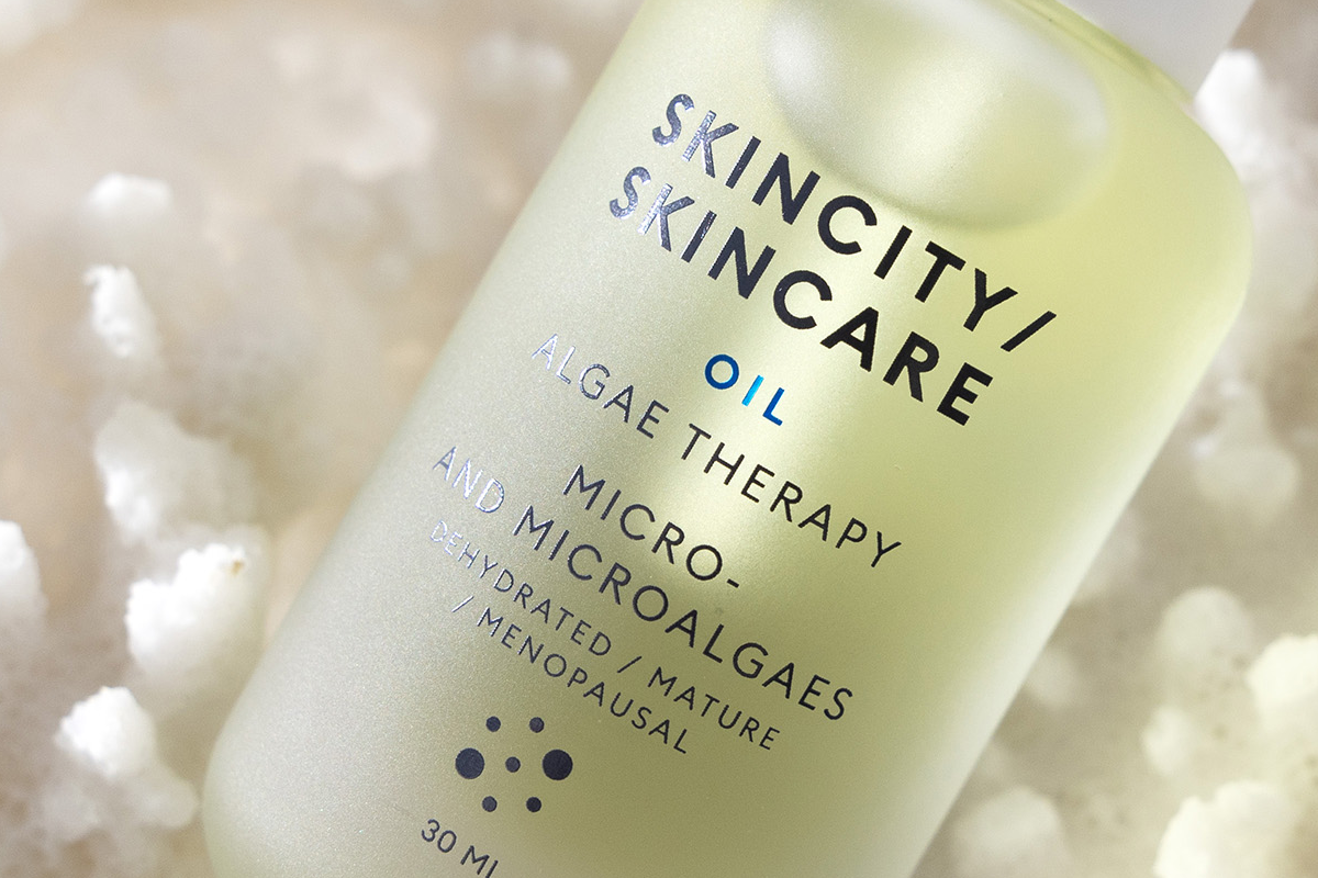 Lähikuva Skincity Skincare Oil Algae Therapy -pullosta valkoisten korallien taustalla.