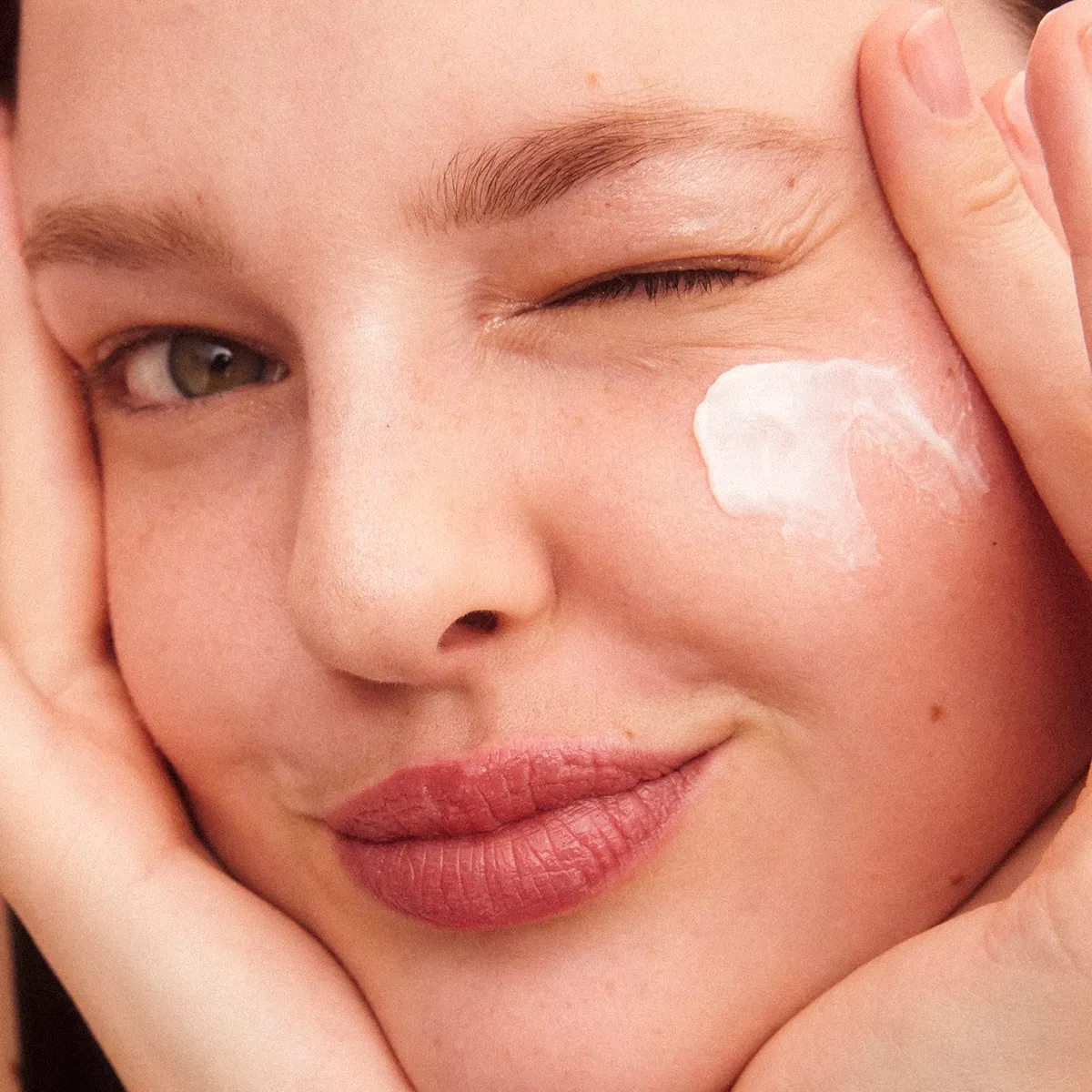 Henkilö pitää kättä kasvojen edessä vaaleanpunaisella taustalla.