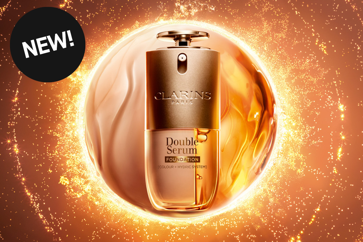 Clarins Double Serum Foundation-flaske omgitt av en gyllen lyssirkel og glitrende partikler. Øverst til venstre en svart sirkel med teksten «NEW!».