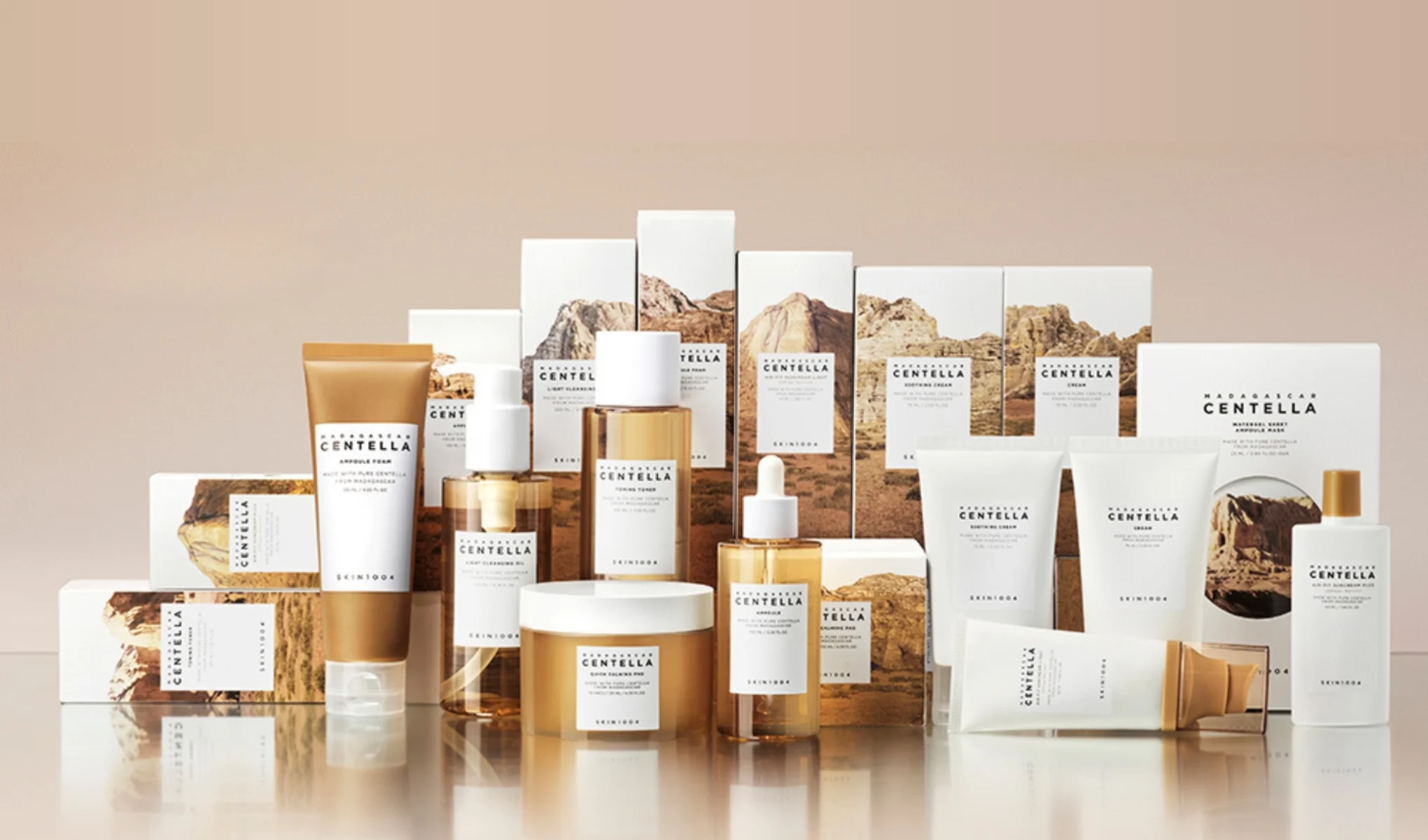 En rad hudvårdsprodukter från märket SKIN1004. De är arrangerade på en ljus yta med sina förpackningar i bakgrunden, som har bilder av berg och natur. Bakgrunden är beige och skapar en harmonisk och naturlig känsla.