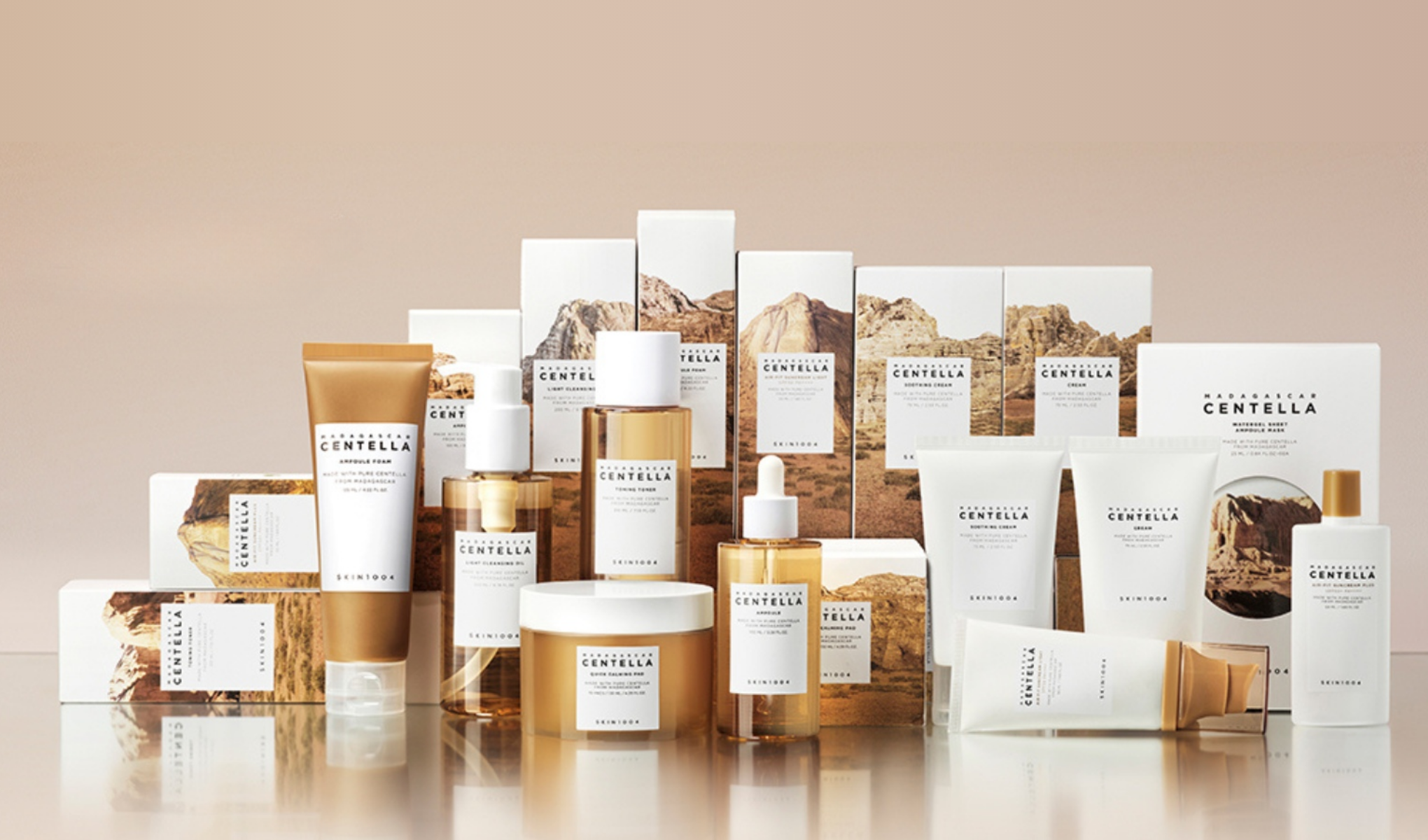 SKIN1004-brändin ihonhoitotuotteiden valikoima. Tuotteet on järjestetty kirkkaalle pinnalle, ja taustalla on niiden pakkaukset, joissa on kuvia vuorista ja luonnosta. Tausta on beige, mikä luo harmonisen ja luonnollisen tunnelman.