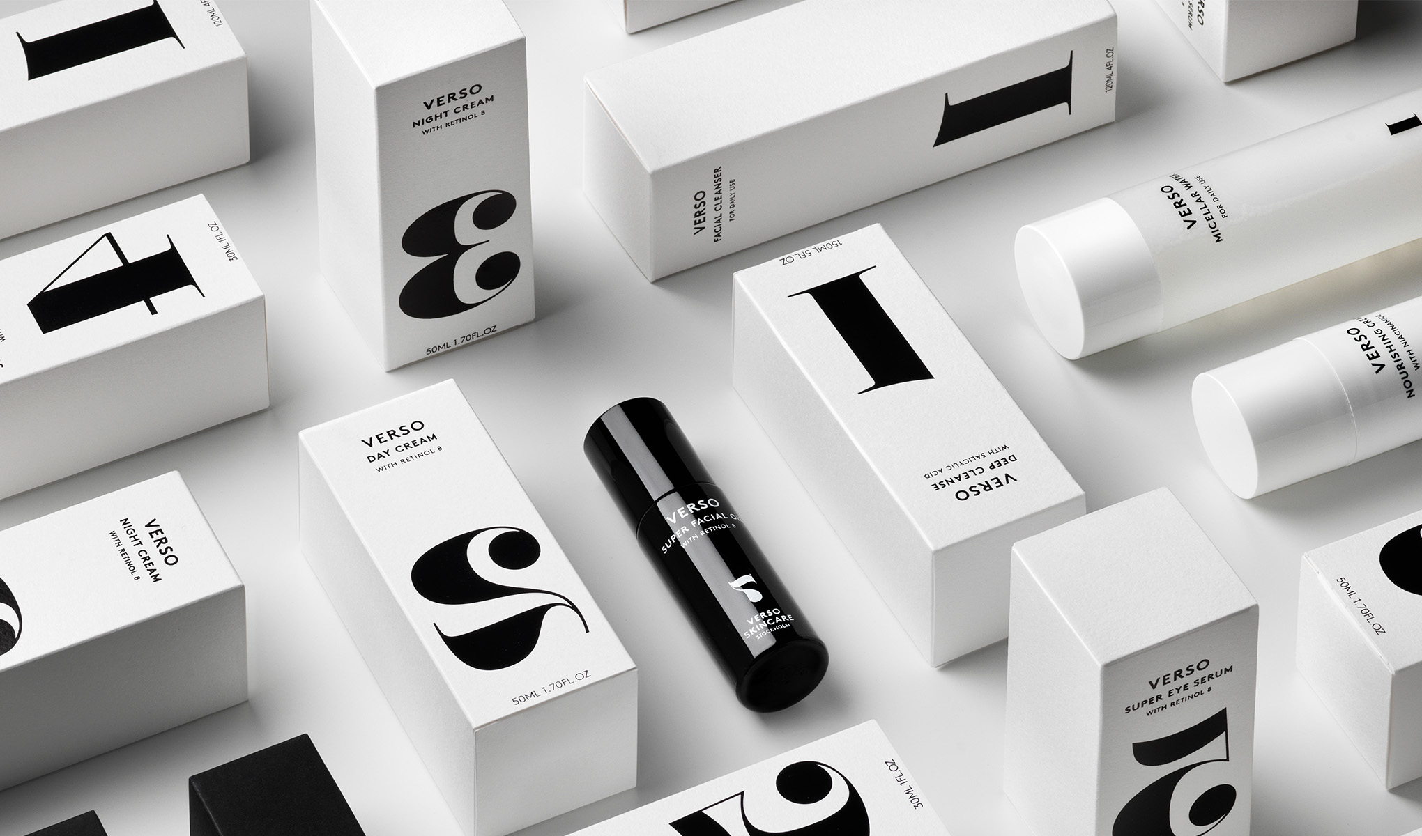 Kokoelma Verso Skincaren ihonhoitotuotteita, jotka on pakattu valkoisiin laatikoihin, joissa on suuret mustat numerot ja kirjaimet. Keskellä on musta pullo, jossa on teksti ”Verso Super Facial Serum”.