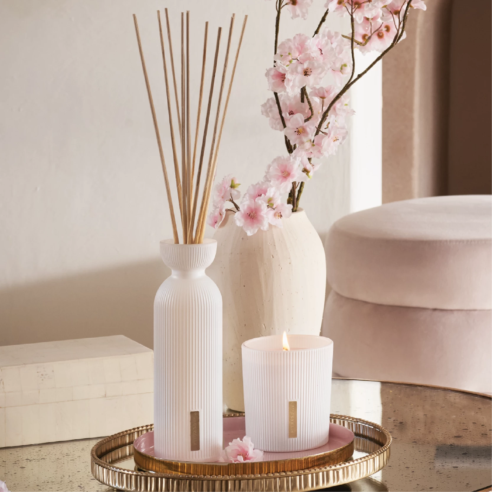 Rituals duftlys og duftpinner og vase med kvistar av blomstrande kirsebær står i eit lyst rom.