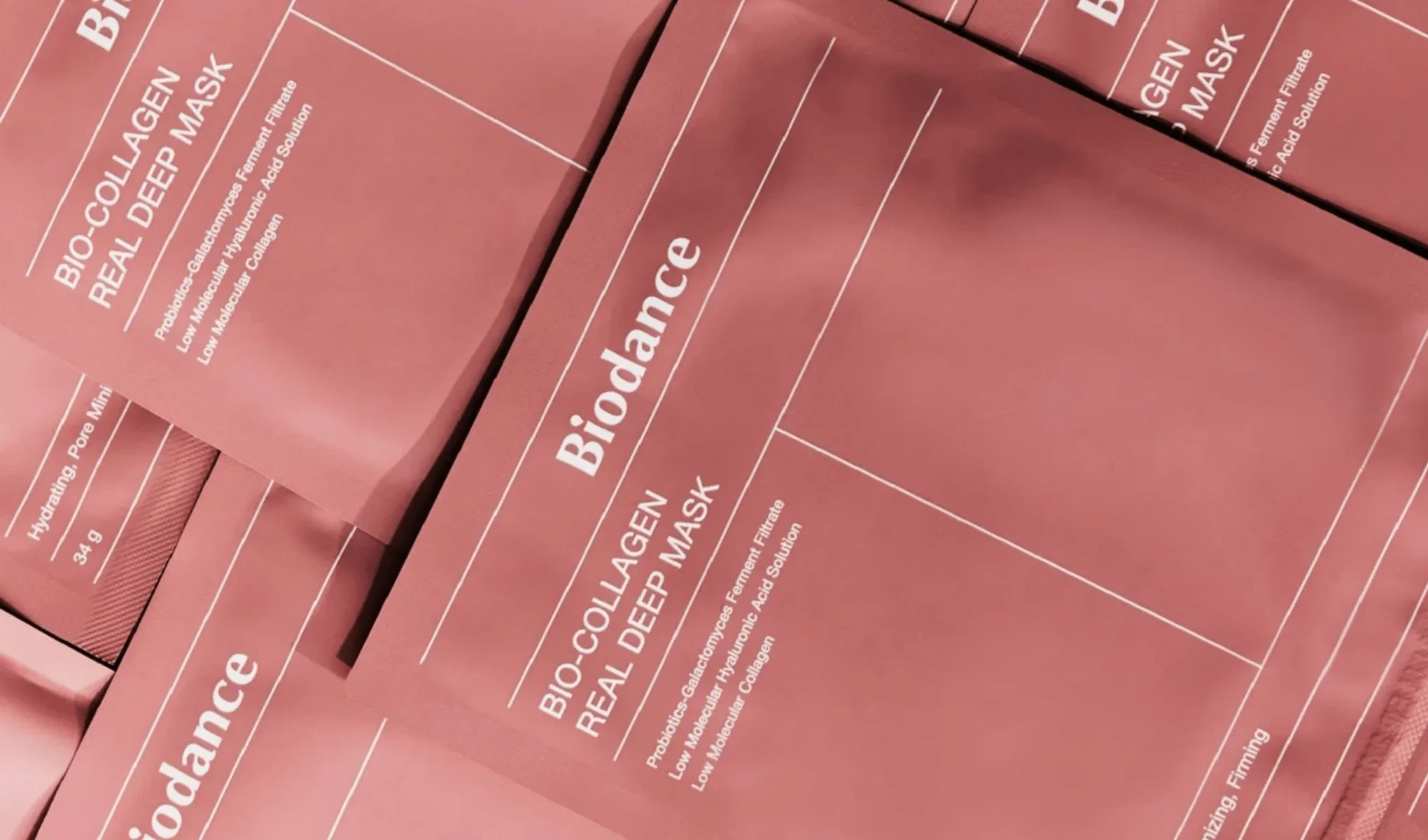 Flere pakker med Biodance Bio-Collagen Real Deep Mask, plassert tett sammen. Pakkene er rosa med hvit tekst som beskriver maskens ingredienser og fordeler. Bakgrunnen er også rosa.