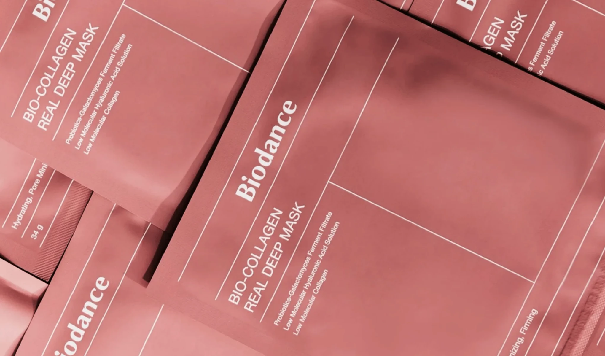 Useita pakkauksia Biodance Bio-Collagen Real Deep Mask -kasvonaamiota, jotka on järjestetty lähekkäin. Pakkaus on vaaleanpunainen, ja siinä on valkoinen teksti, jossa kuvataan naamion ainesosia ja hyötyjä. Tausta on myös vaaleanpunainen.
