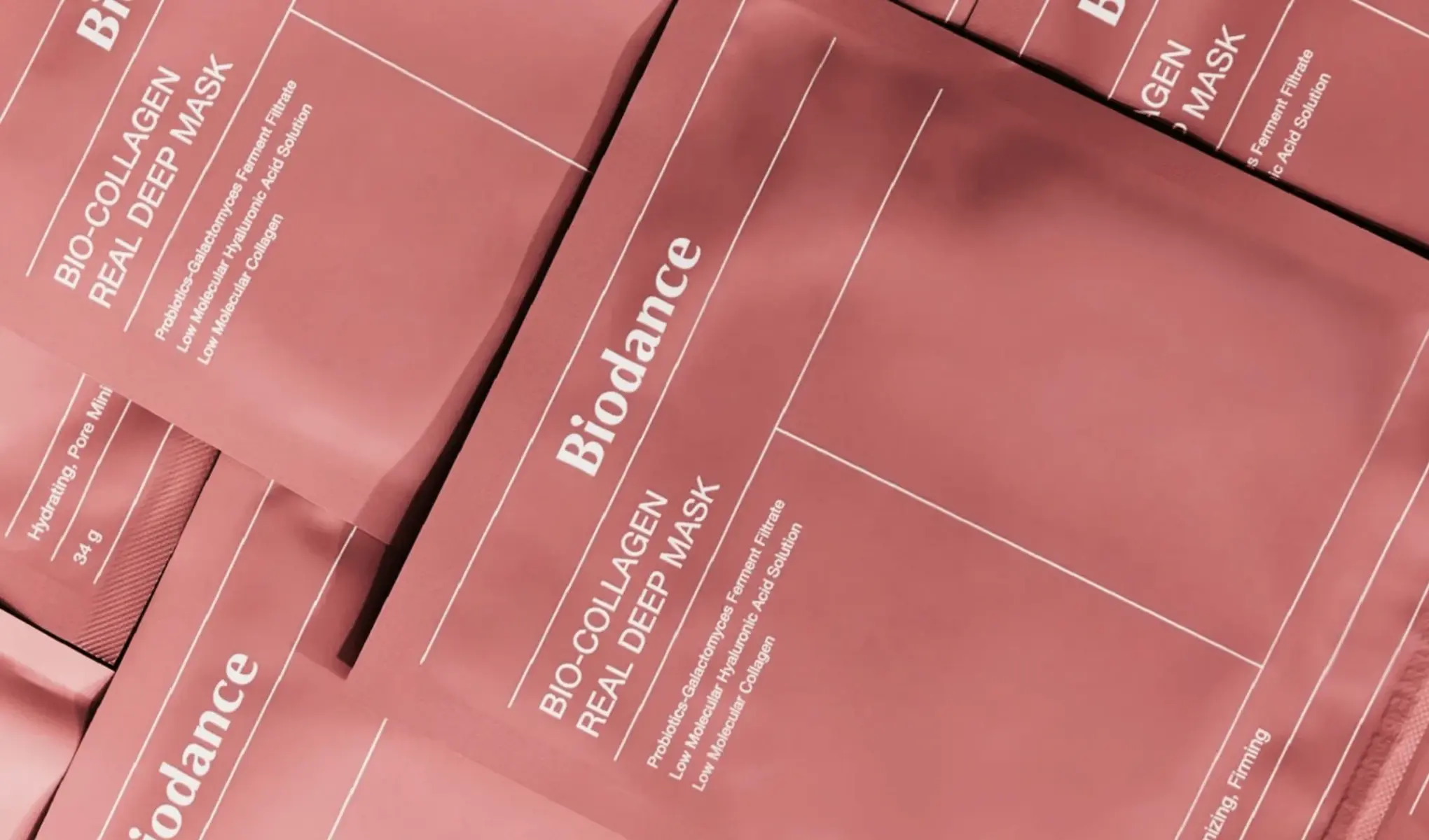 Useita pakkauksia Biodance Bio-Collagen Real Deep Mask -kasvonaamiota, jotka on järjestetty lähekkäin. Pakkaus on vaaleanpunainen, ja siinä on valkoinen teksti, jossa kuvataan naamion ainesosia ja hyötyjä. Tausta on myös vaaleanpunainen.