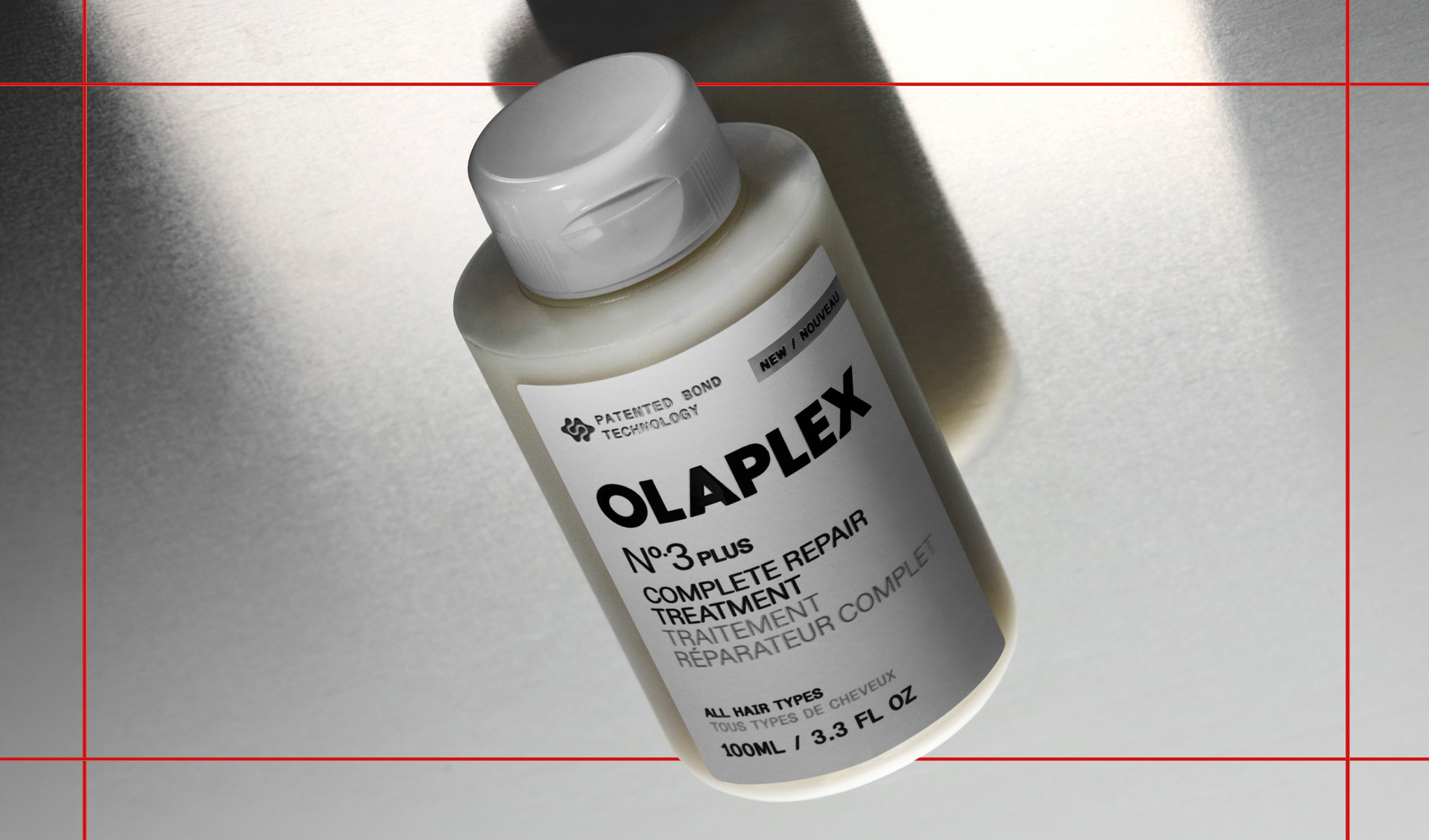 Hårpleieprodukt OLAPLEX No.3 Plus Complete Repair Treatment i en hvit flaske mot lys bakgrunn med skygger. På emballasjen vises tekstene “PATENTED BOND TECHNOLOGY”, “NEW”, “OLAPLEX No.3 PLUS”, “COMPLETE REPAIR TREATMENT”, “ALL HAIR TYPES” og “100ML / 3.3 FL OZ”.