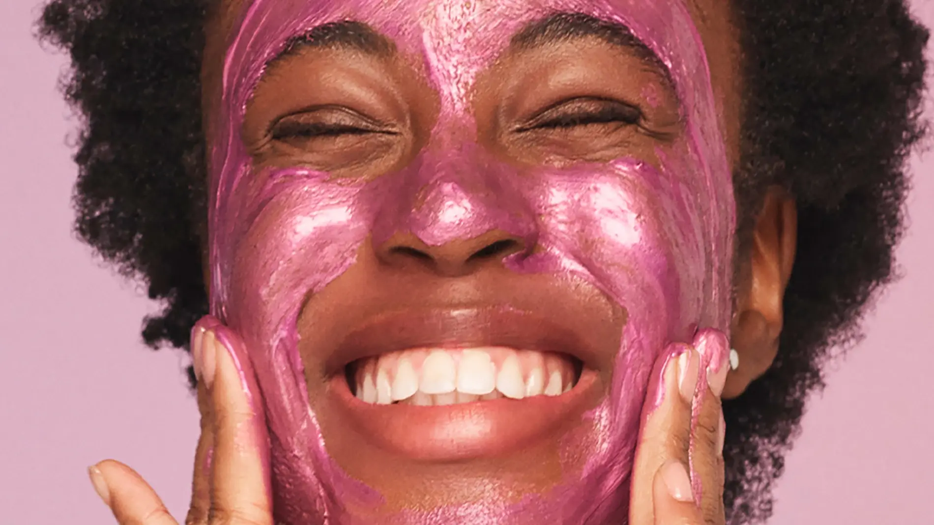 Leende person applicerar en glittrig rosa ansiktsmask.