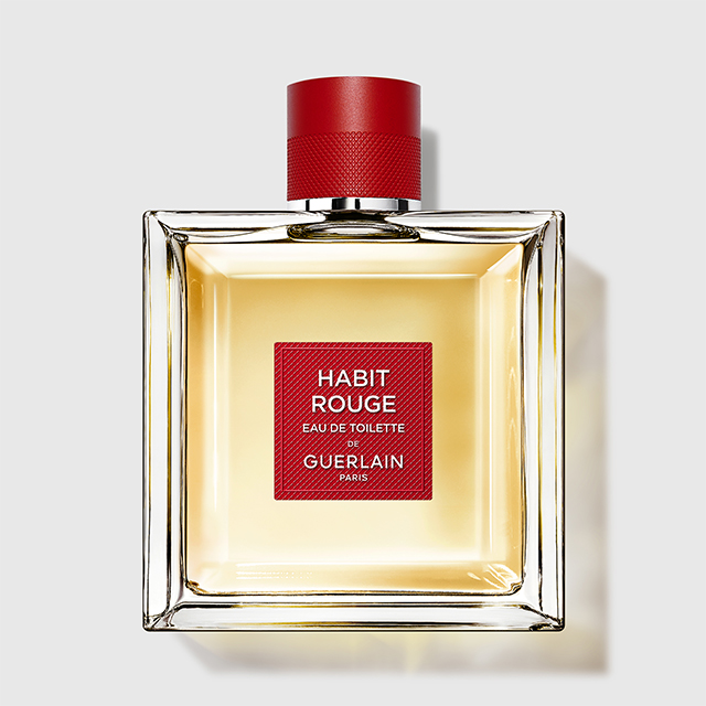Guerlain Habit Rouge Eau de Toilette parfyme i en firkantet glassflaske med lys gyllen væske og rød kork. På forsiden er en rød etikett med teksten “HABIT ROUGE EAU DE TOILETTE GUERLAIN PARIS”.