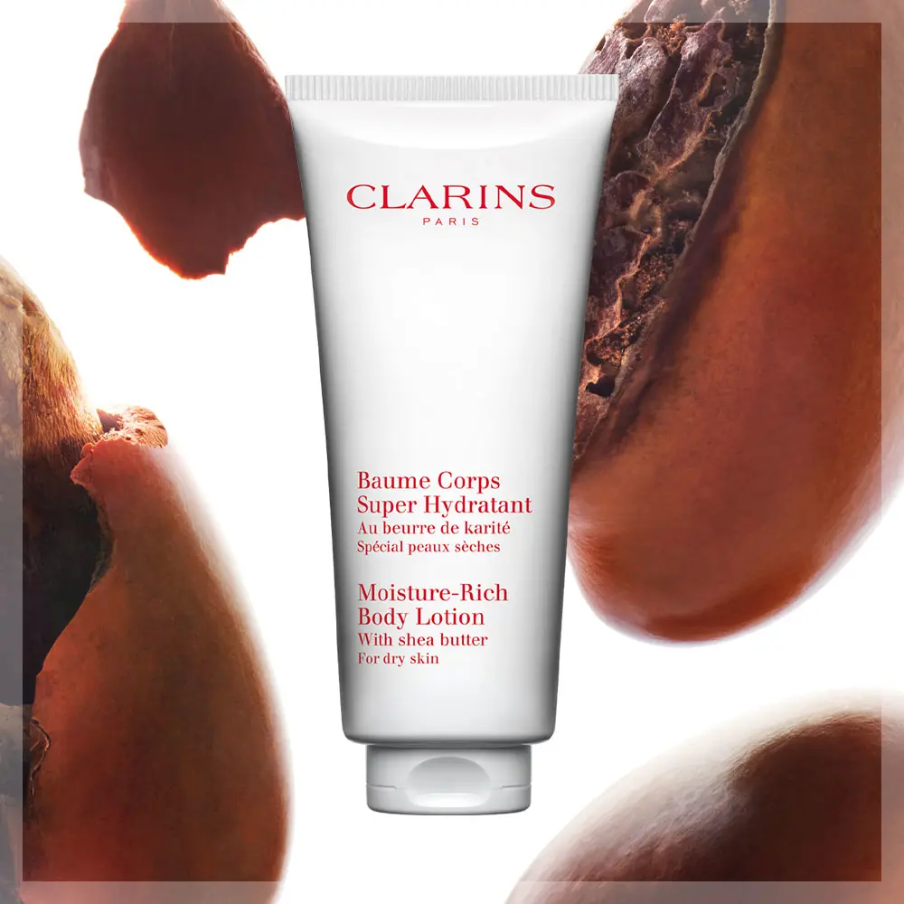 Clarinsin tuote ”Baume Corps Super Hydratant” , taustalla sheapähkinöitä. Tuotteen teksti on sekä ranskaksi että englanniksi, ja se kuvaa tuotetta kosteuttavaksi vartalovoiteeksi kuivalle iholle.