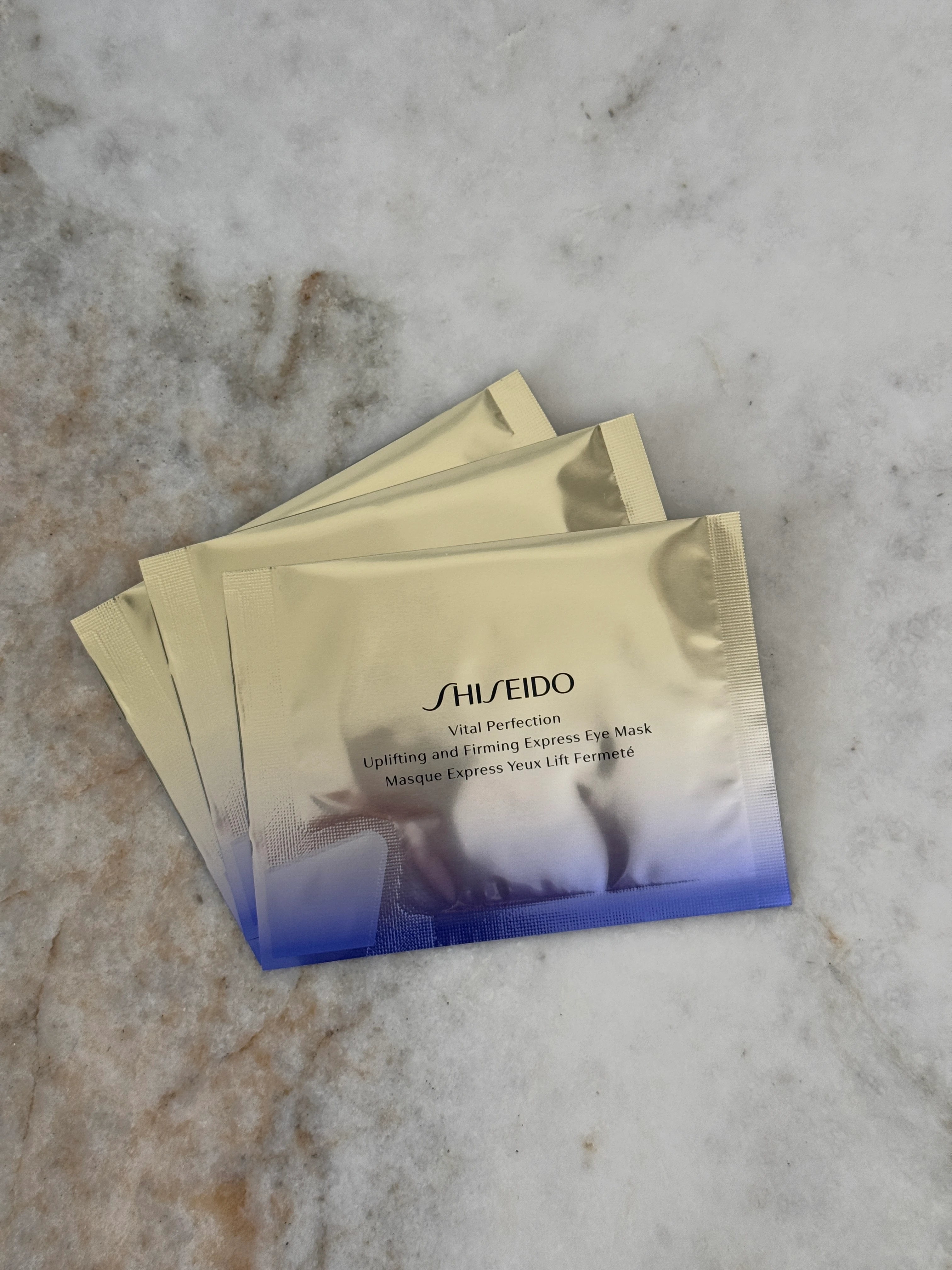 Kolme pakkausta Shiseidon Uplifting and Firming Express Eye Mask -silmänaamioita, aseteltuna marmorialustalle.