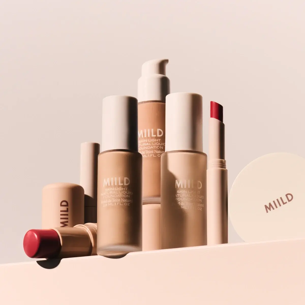 Sminkeprodukter fra MIILD mot en lys bakgrunn, blant annet foundation, blush og leppeprodukt.