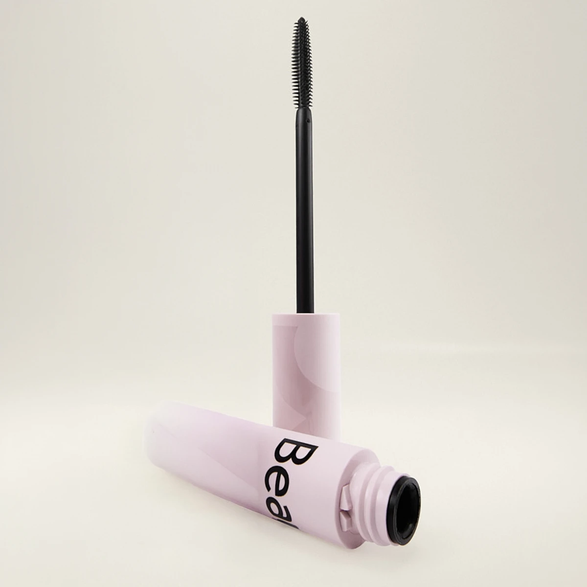 Öppen mascara från BeautyAct med ljusrosa hylsa och svart borste applicator mot ljus bakgrund, med synlig text “Bea” på förpackningen.