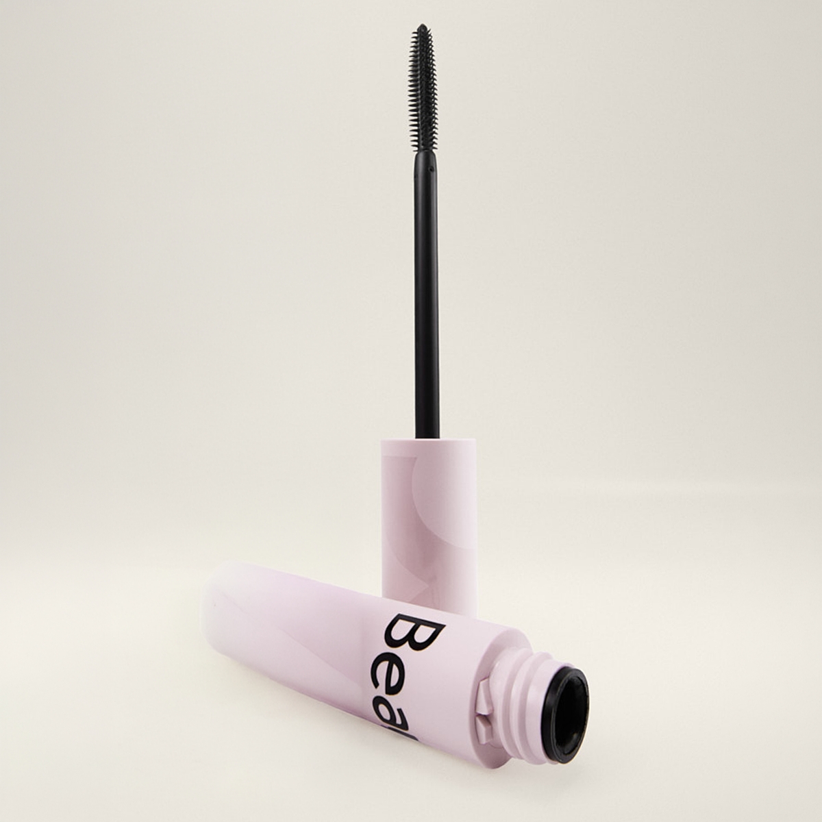 Åpen mascara fra BeautyAct med lys rosa hylse og svart børsteapplikator mot lys bakgrunn, med synlig tekst “Bea” på emballasjen.