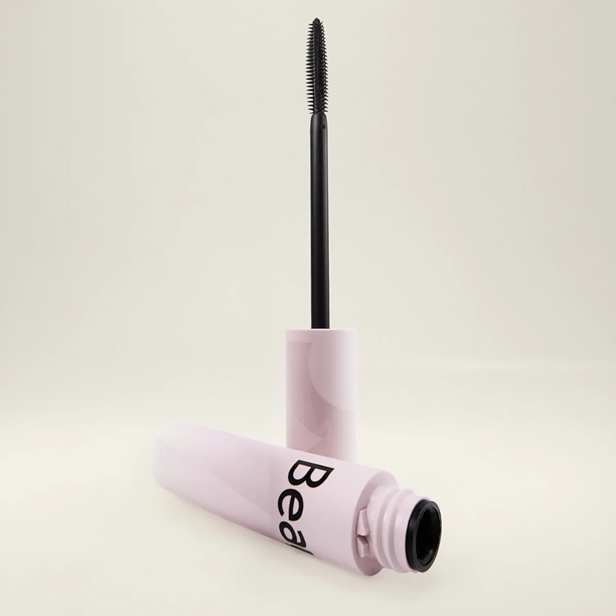 Åpen mascara fra BeautyAct med lys rosa hylse og svart børsteapplikator mot lys bakgrunn, med synlig tekst “Bea” på emballasjen.