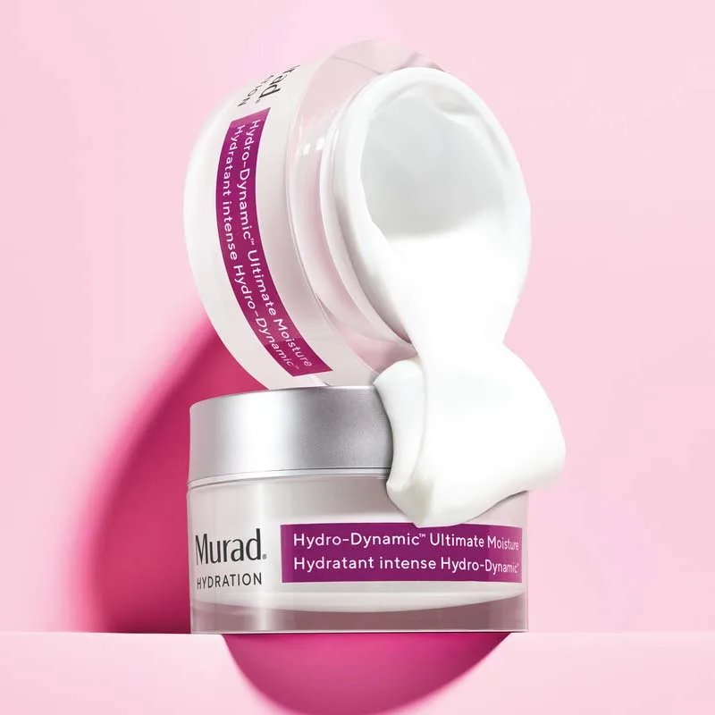 Två burkar nattkräm från Murad. Den ena brukar är öppen med vit kräm är placerad ovanpå en annan burk mot en rosa bakgrund. Den övre burken har en lila etikett som visar produktnamnet och krämens innehåll rinner ner över den nedre burken, vilket framhäver dess rika och återfuktande konsistens.