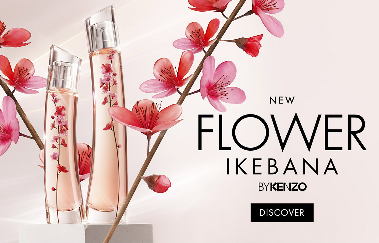 Kaksi hajuvesipulloa Kenzon ”Flower Ikebana” -mallistosta vaaleaa taustaa vasten. Pullot on koristeltu vaaleanpunaisilla kukilla, ja niitä ympäröivät kukkivat oksat. Kuvassa on teksti: ”New Flower Ikebana by Kenzo” ja ”Discover”.