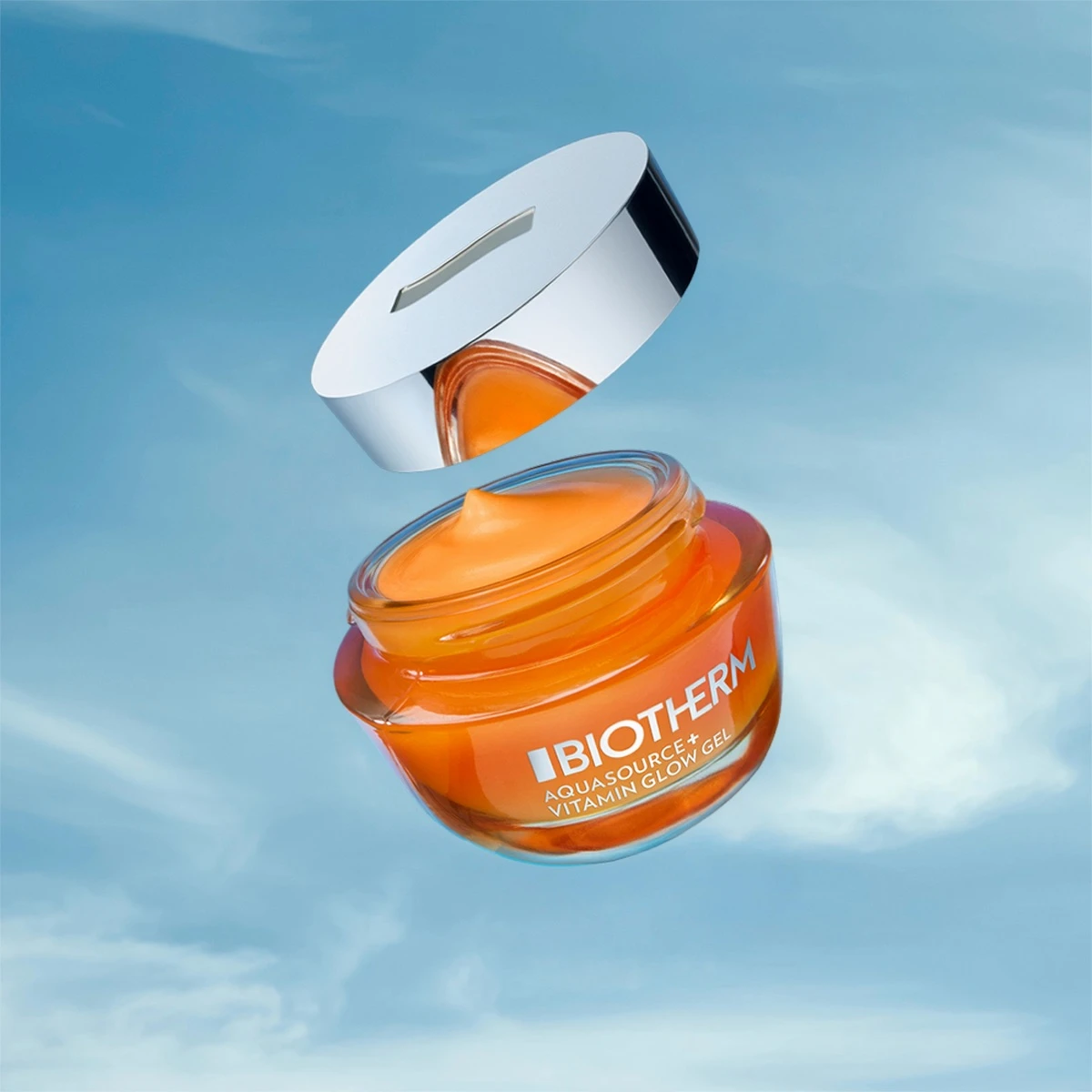 Biotherm Aquasource+ Vitamin Glow Gel i en orange burk med silverlock, svävande mot en blå himmel.