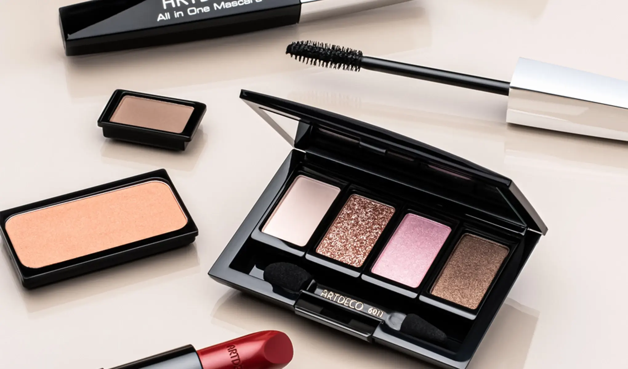 Artdeco sminkeprodukter, inkludert en øyenskyggepalett med fire farger, en mascara, en leppestift, en rouge og en enkelt øyenskygge. Produktene er arrangert på en lys overflate.
