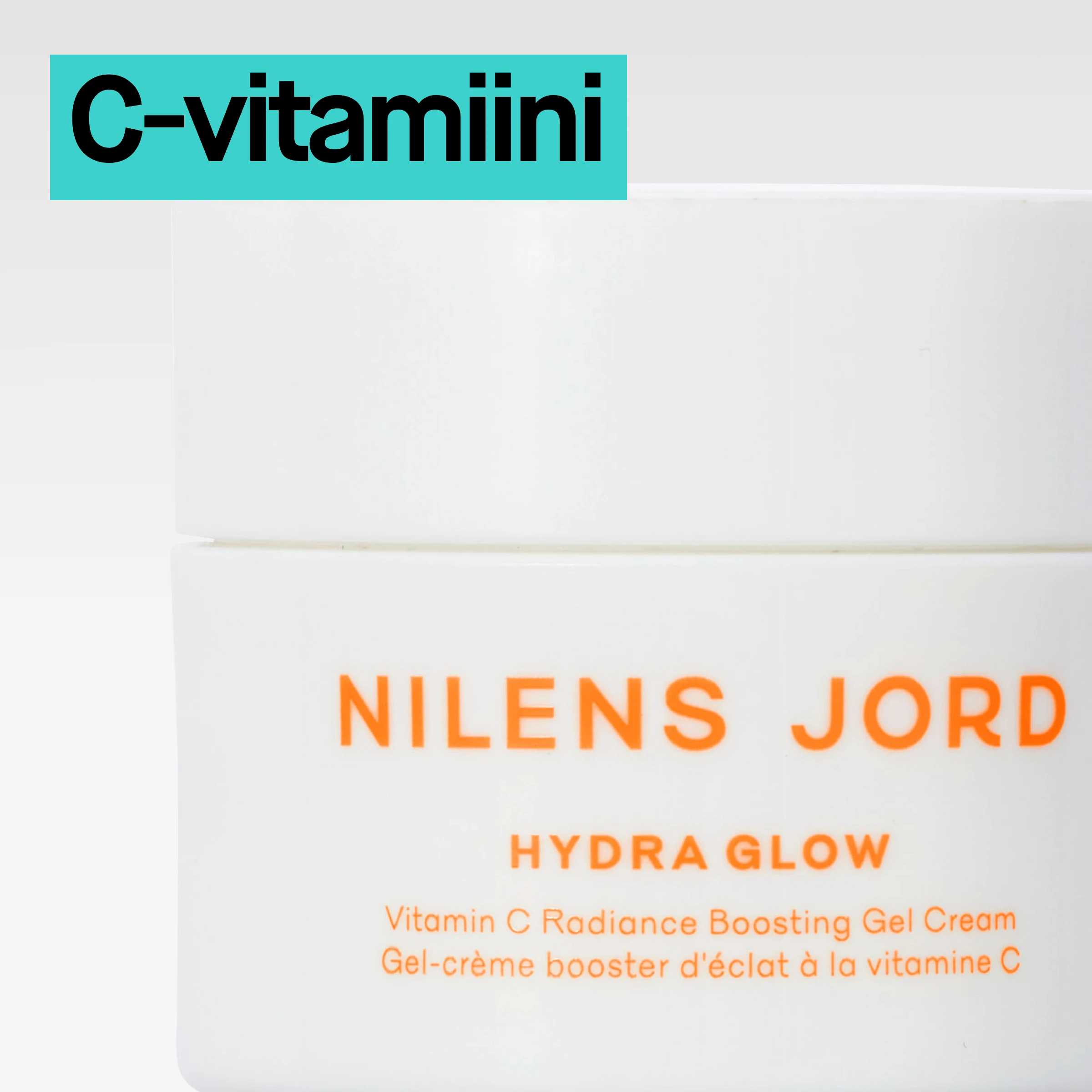 Valkoinen purkki, jossa oranssi teksti ”Nilens Jord Hydra Glow Vitamin C Radiance Boosting Gel Cream”, lähikuvassa vaaleaa taustaa vasten ja turkoosi ”C-vitamin”-merkintä.