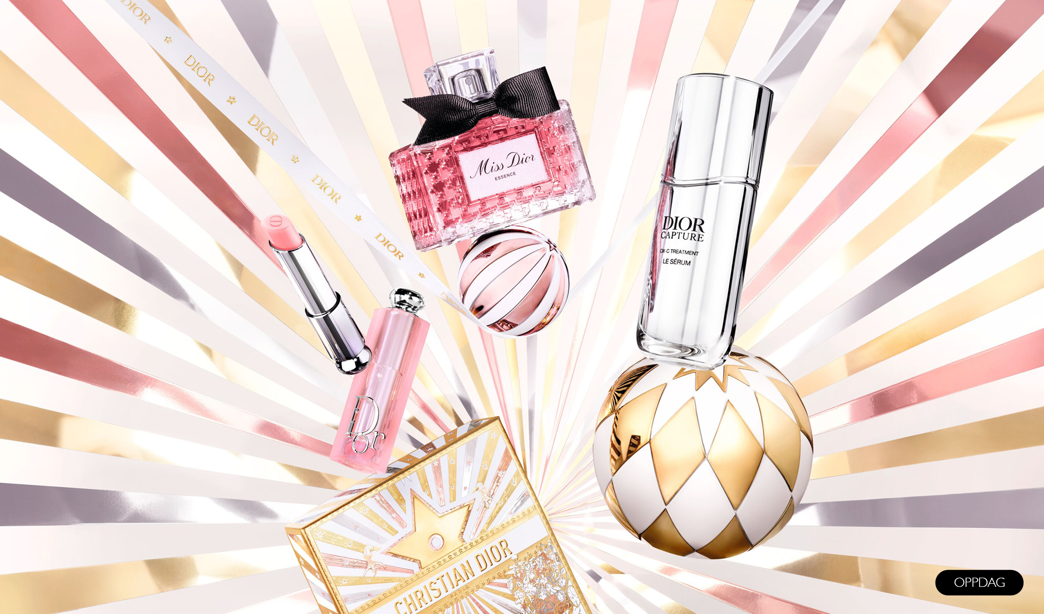 En samling Dior-produkter, inkludert parfyme, leppestift og serum, arrangert mot en bakgrunn med strålende linjer i gull, rosa og hvitt. Produktene er elegant plassert sammen med en dekorativ kule og en gaveeske.