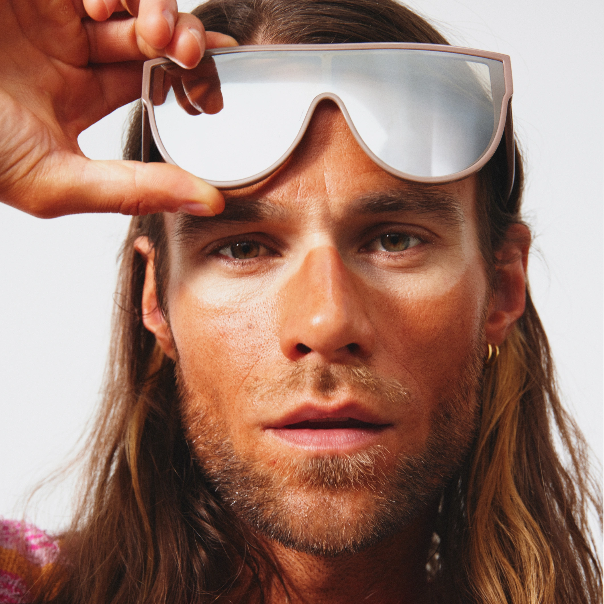 Närbild på person med solbrun ton i ansiktet som håller upp stora ljusa solglasögon. Texten ”Self tan ansikte” visas i svart ruta.