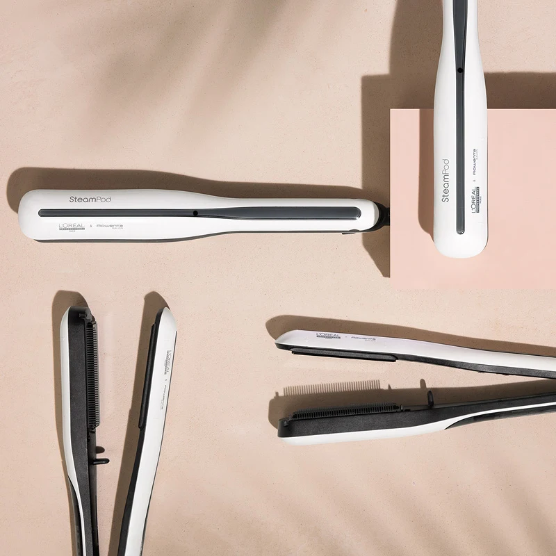 Viisi valkoista L'Oréal Professionnel SteamPod -suoristuslaitetta on levitetty beigeen pintaan. Osa suoristusraudoista on avoinna ja osa kiinni. Taustalla on varjostettu vaikutus.