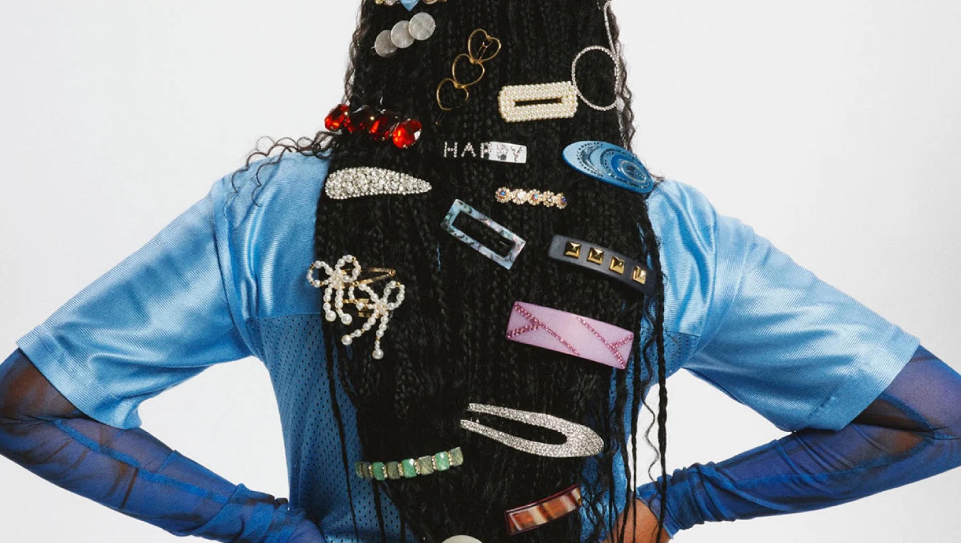 Pitkät tummat letit, jotka ovat täynnä värikkäitä ja kimaltelevia hiusklipsejä, joista yhdessä lukee "HAPPY".