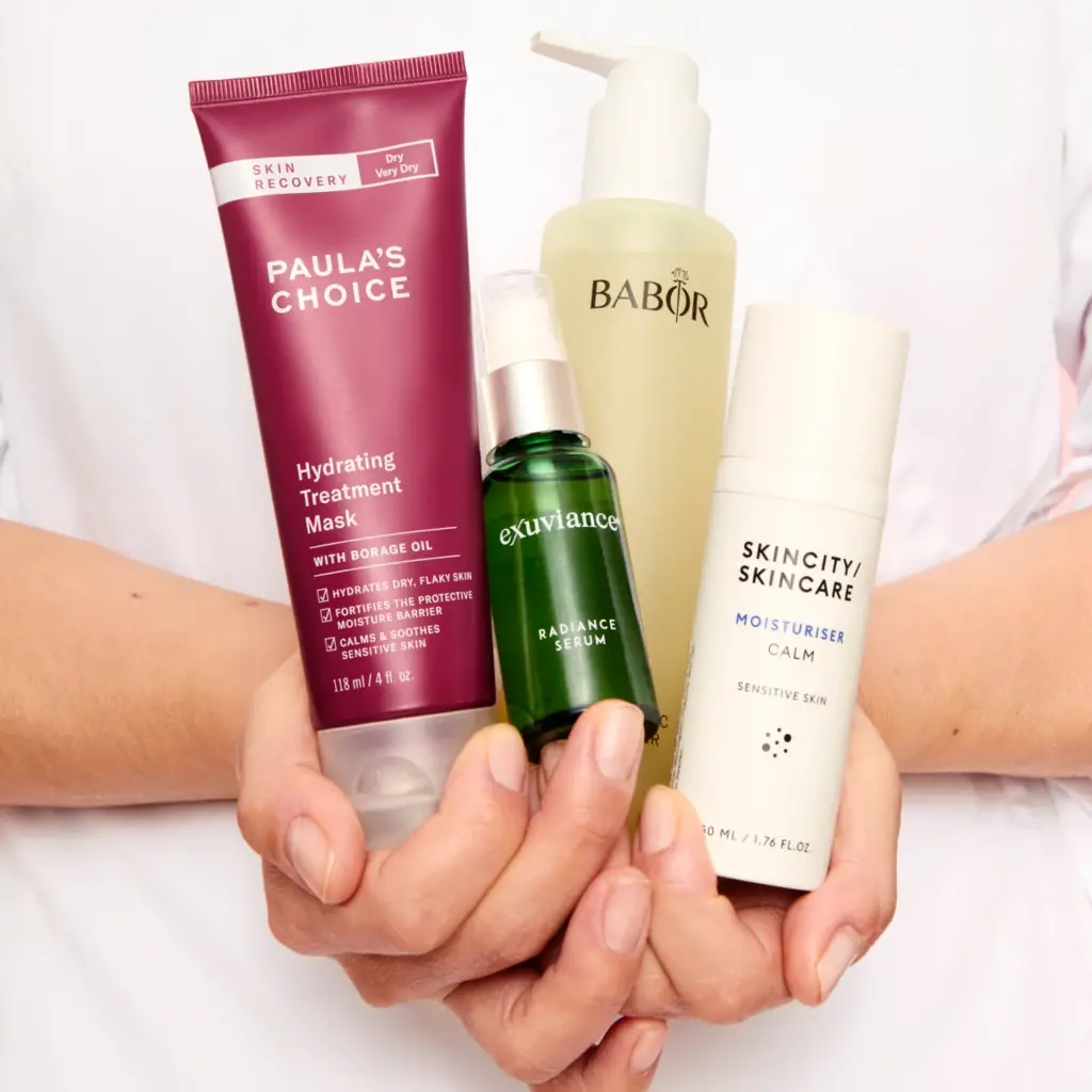 En person holder fire hudpleieprodukter: Paula's Choice Hydrating Treatment Mask, Babor rensegel, Exuviance Radiance Serum og Skincity Skincare Moisturiser Calm.