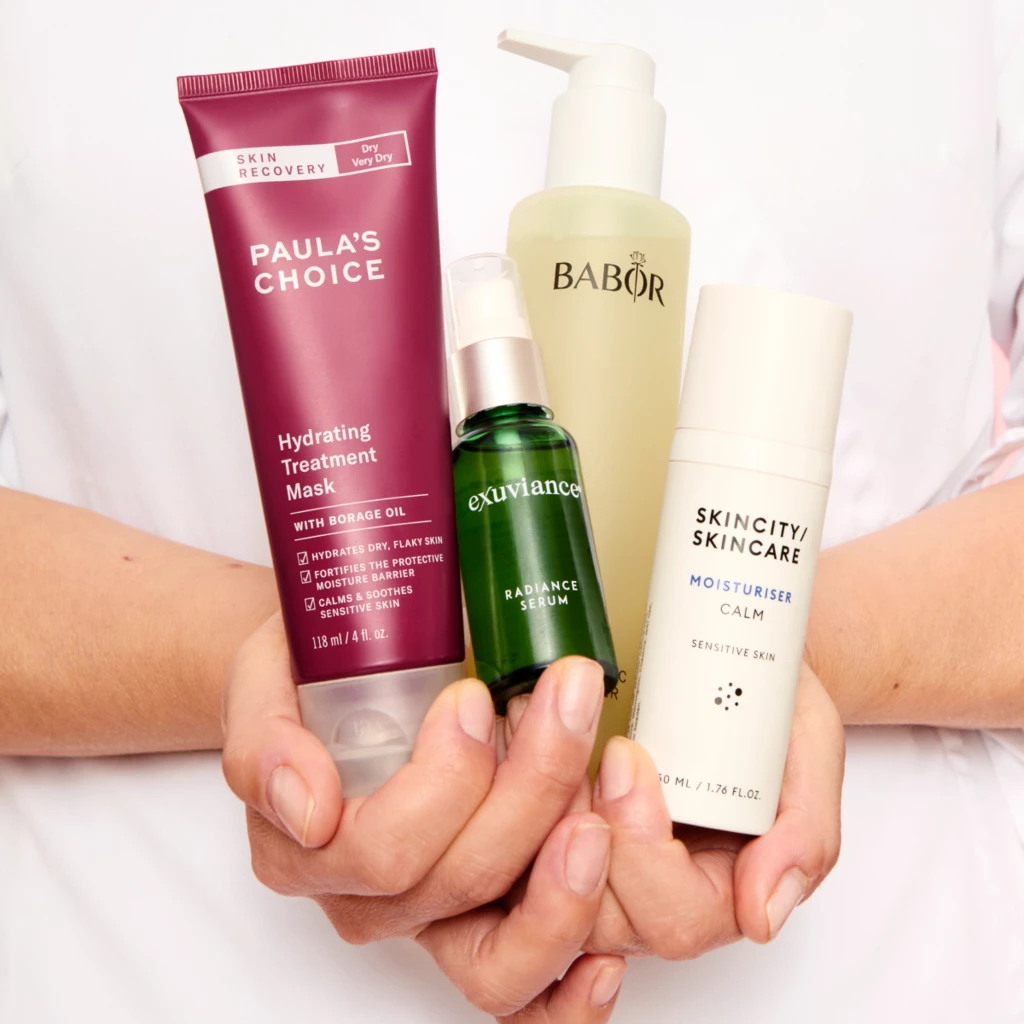 En person håller fyra hudvårdsprodukter: Paula's Choice Hydrating Treatment Mask, Babor rengöringsgel, Exuviance Radiance Serum och Skincity Skincare Moisturiser Calm.
