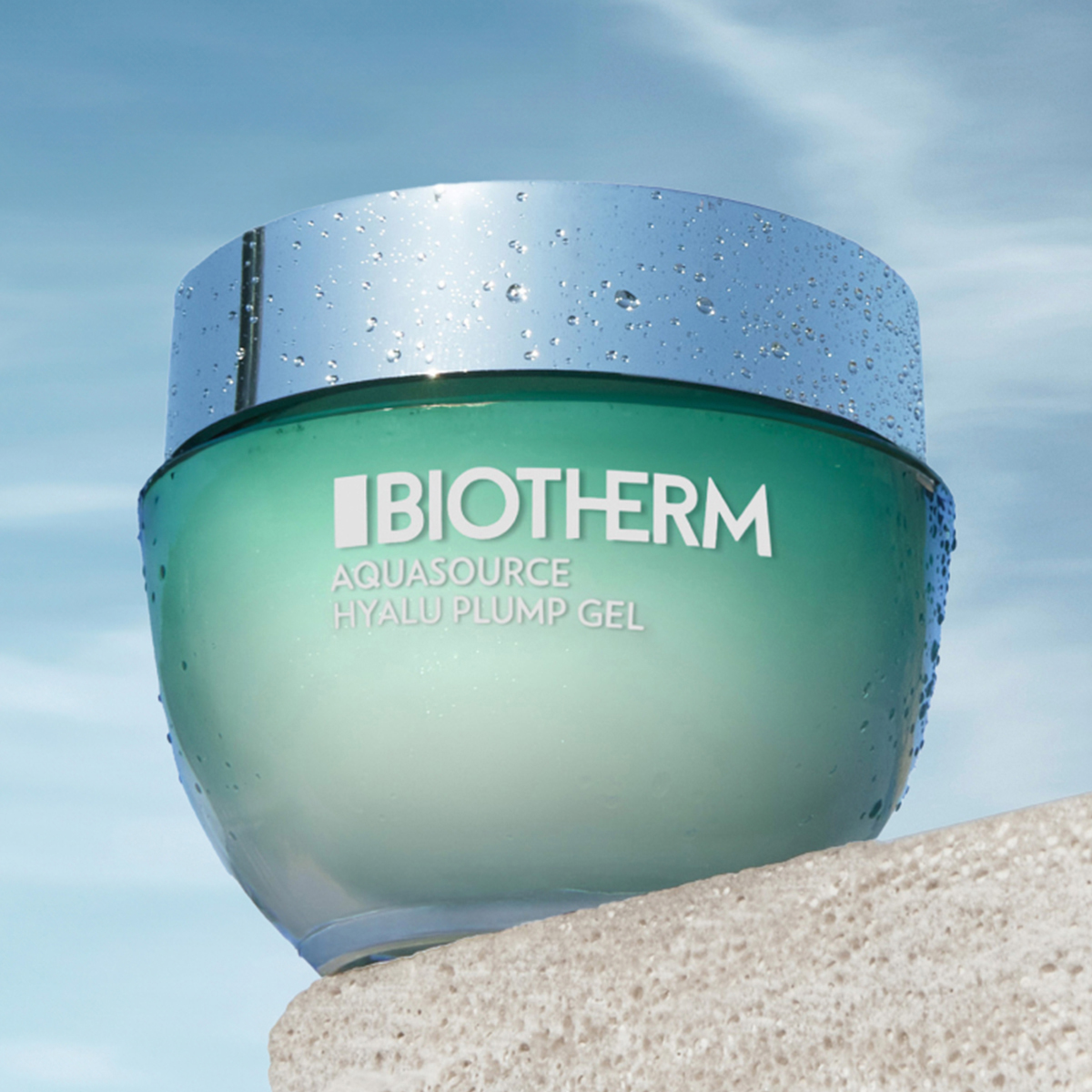 Aquasource Hyalu Plump -geeli Biothermiltä. Geeli on vihreässä lasipurkissa, jossa on hopeinen kansi ja jonka etupuolella on teksti ”Biotherm Aquasource Hyalu Plump Gel”. Purkki seisoo beigen värisellä alustalla sinistä taivasta vasten, jossa on joitakin valkoisia pilviä.