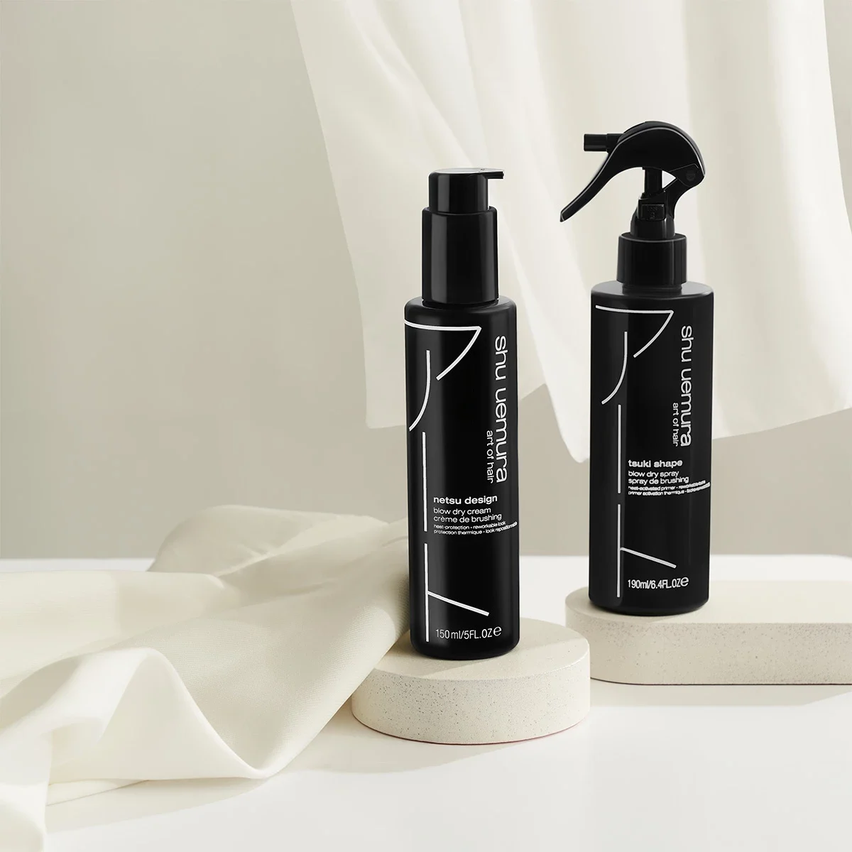 Två svarta flaskor med hårvårdsprodukter från Shu Uemura. Den ena flaskan har en pump och den andra en spraymunstycke. Bakgrunden är enkel och ren.