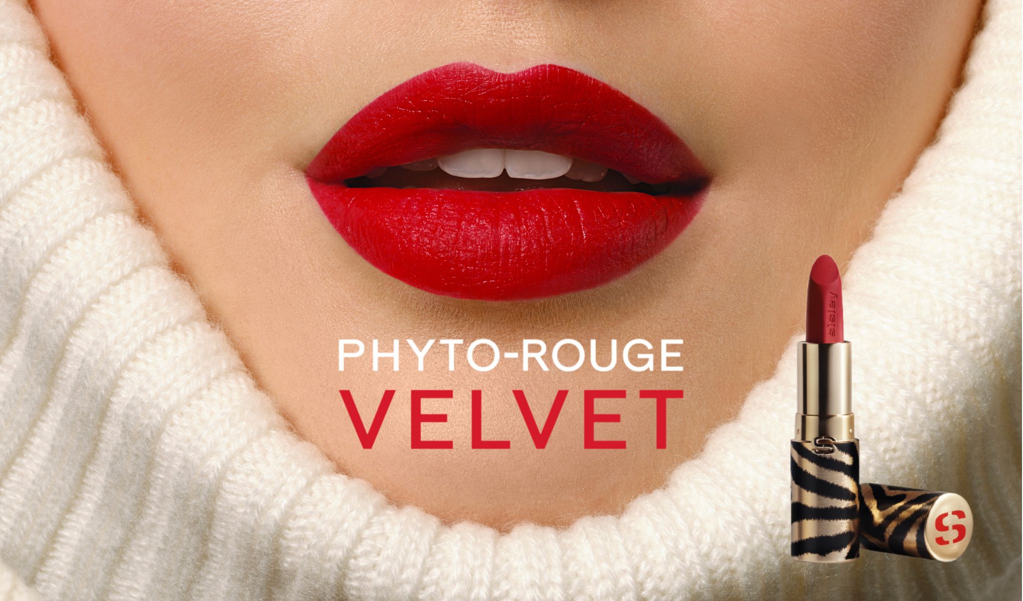 Närbild på en kvinnas läppar målade med rött läppstift, omgiven av en vit stickad tröja. Texten "Phyto-Rouge Velvet" är placerad under läpparna, och en bild av läppstiftet med zebramönstrat hylsa visas till höger.