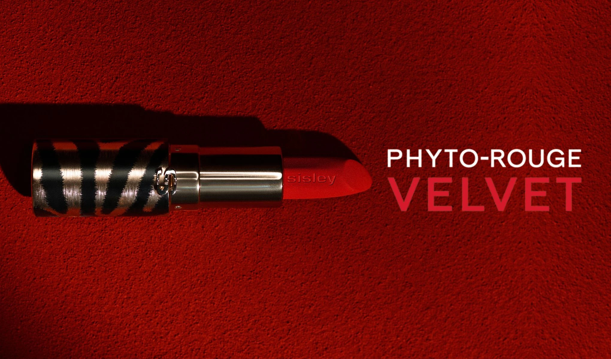 En rød leppestift fra Sisley med sebramønstret hylse på rød bakgrunn. Teksten «Phyto-Rouge Velvet» er plassert til høyre for leppestiften.