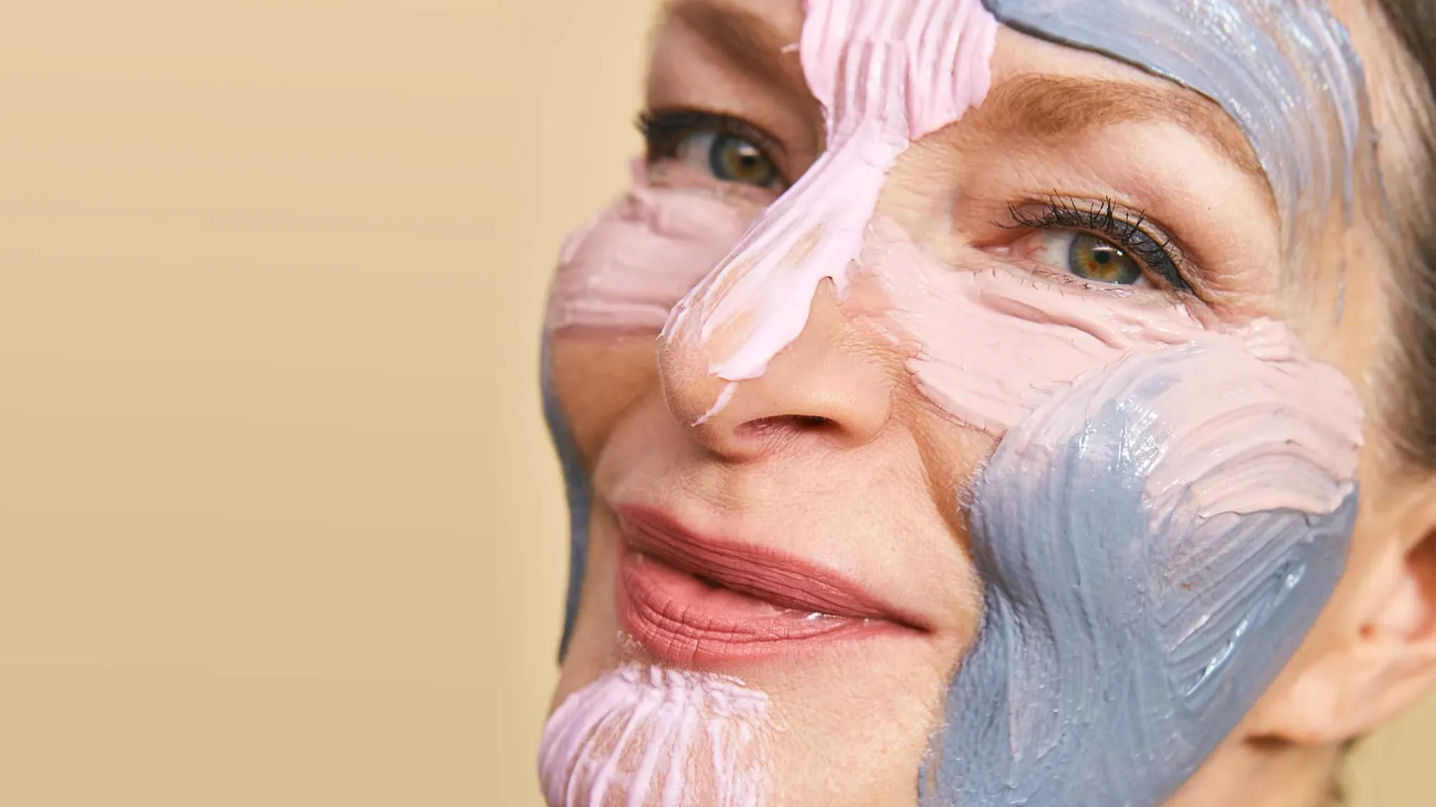 Närbild av kvinna med mogen hud som applicerat färgglada ansiktsmasker i olika zoner i ansiktet