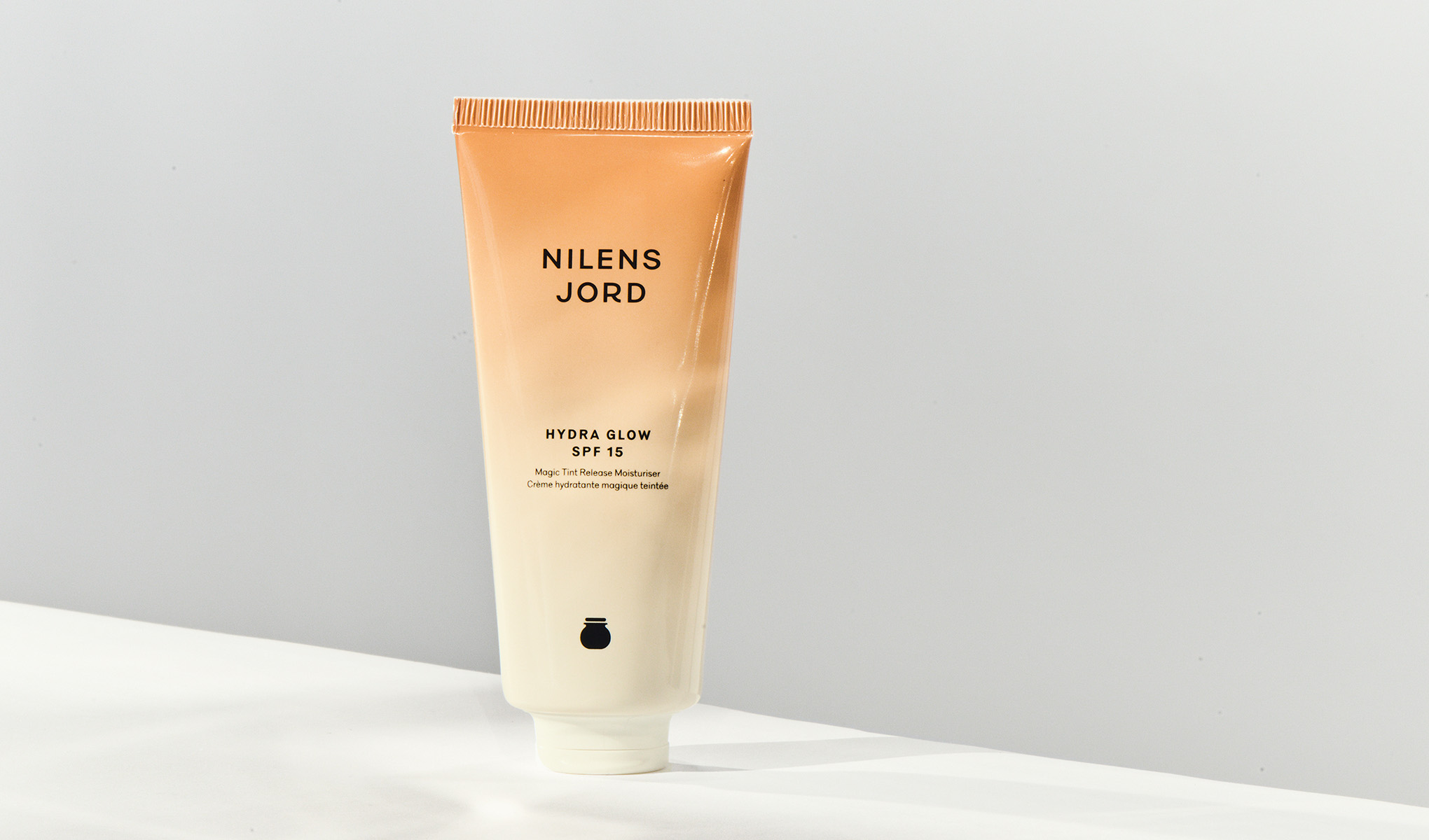 Nilens Jord Hydra Glow SPF 15 fuktighetskrem. Tuben er lys oransje og hvit, med svart tekst.