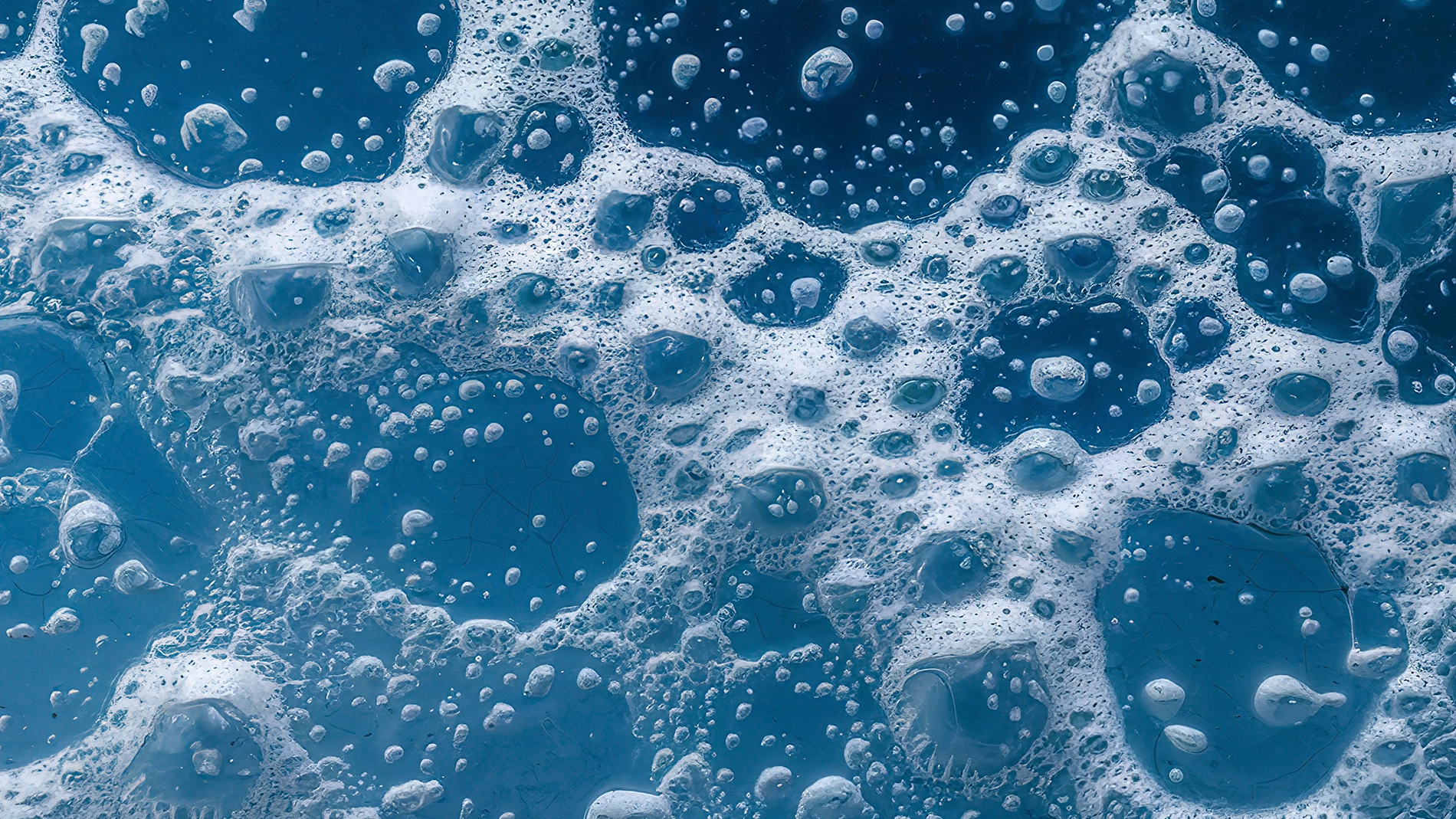 Lähikuva sinisestä nesteestä, jossa erikokoisia vaahtokuplia muodostaa abstraktin kuvion, viittaa puhdistukseen tai ihonhoitoon kuten kasvojenpuhdistusaineeseen tai geeliin.