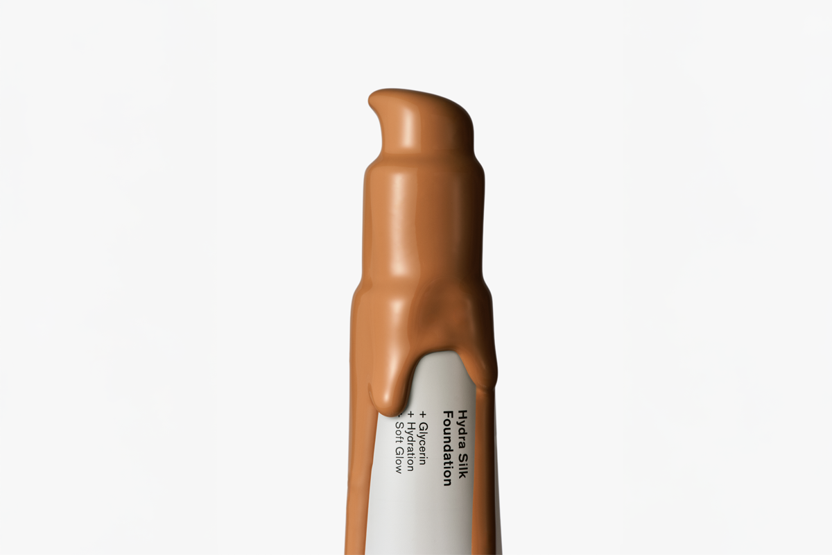 Närbild på en brun BeautyAct Hydra Silk Foundation i pumpförpackning mot vit bakgrund. På förpackningen står ”Hydra Silk Foundation”, ”+ Glycerin”, ”+ Hydration” och ”+ Soft Glow”.