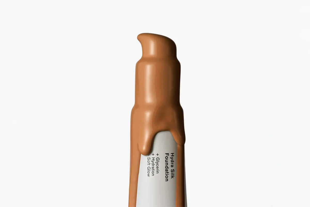 Närbild på en brun BeautyAct Hydra Silk Foundation i pumpförpackning mot vit bakgrund. På förpackningen står ”Hydra Silk Foundation”, ”+ Glycerin”, ”+ Hydration” och ”+ Soft Glow”.